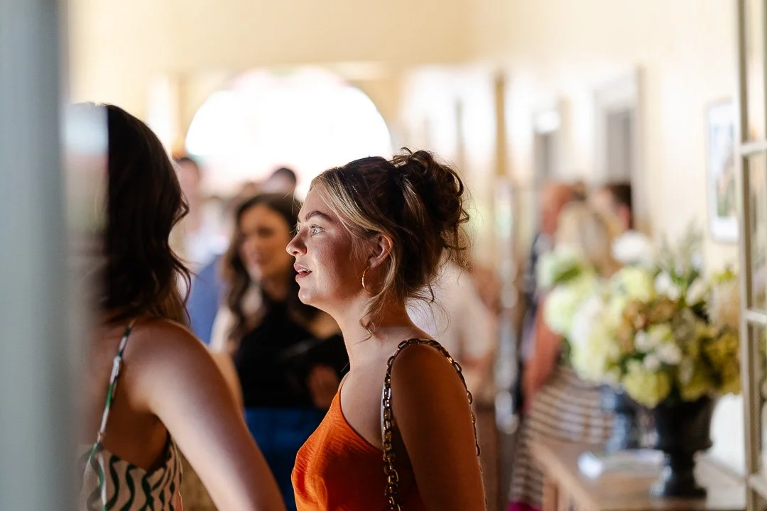 Guests standing and looking towards a window with natural light shining through on to her face at a Hampton Court House Wedding.