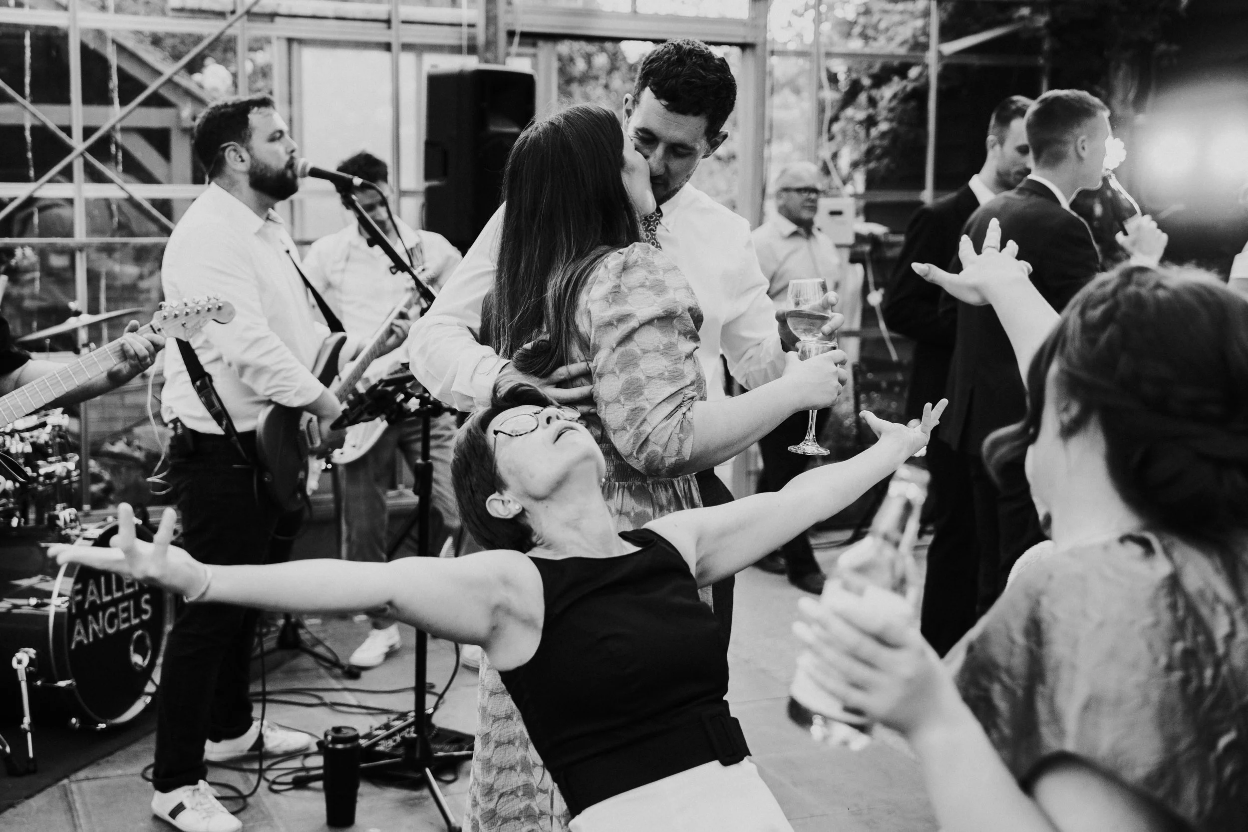 Wedding guests kissing on dancefloor while another guest is posing with her arms wide open at a Worton Kitchen Garden, Oxfordshire Wedding.