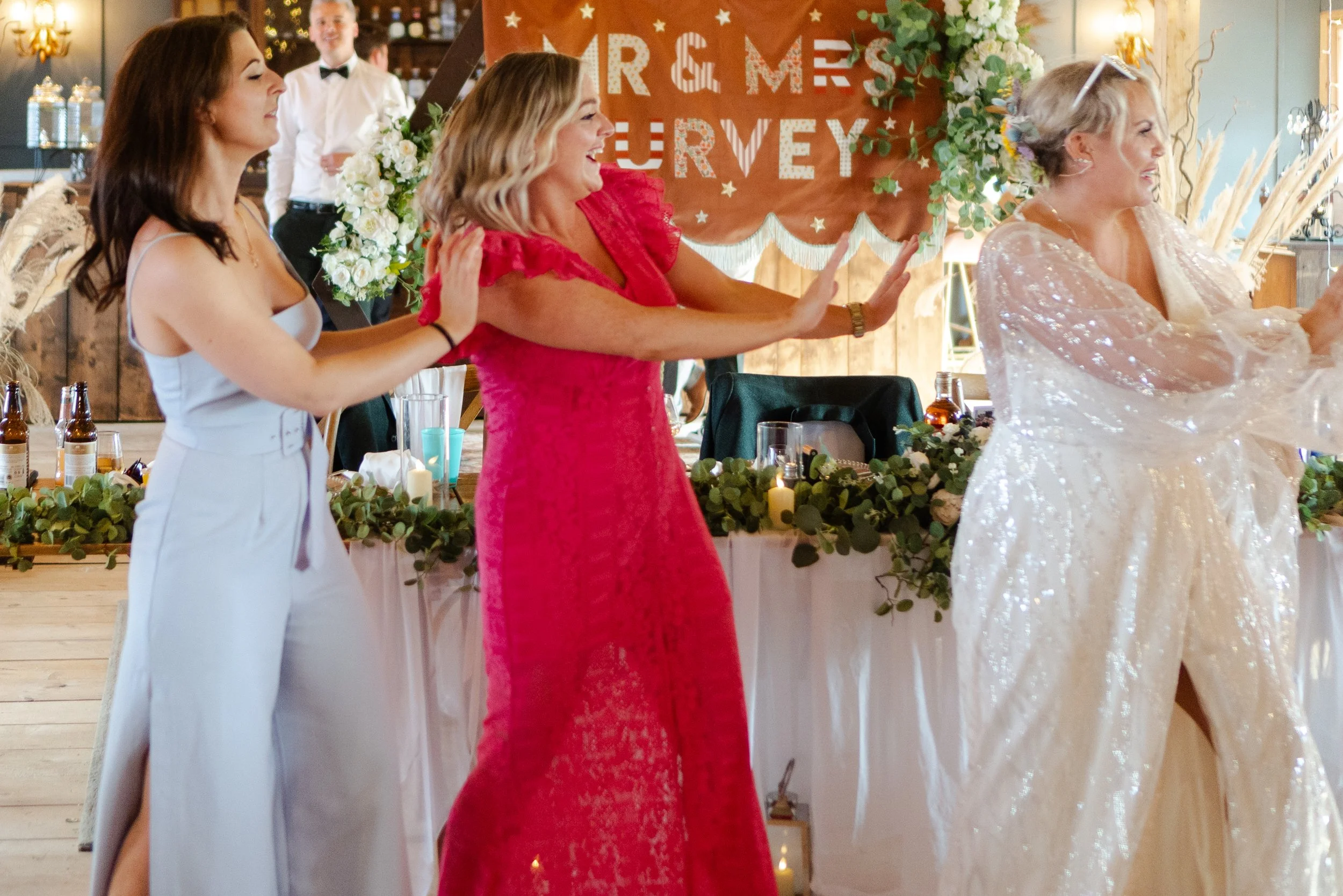 Bride and two wedding guests dancing in a line in front of the top table at a rhyse farm wedding