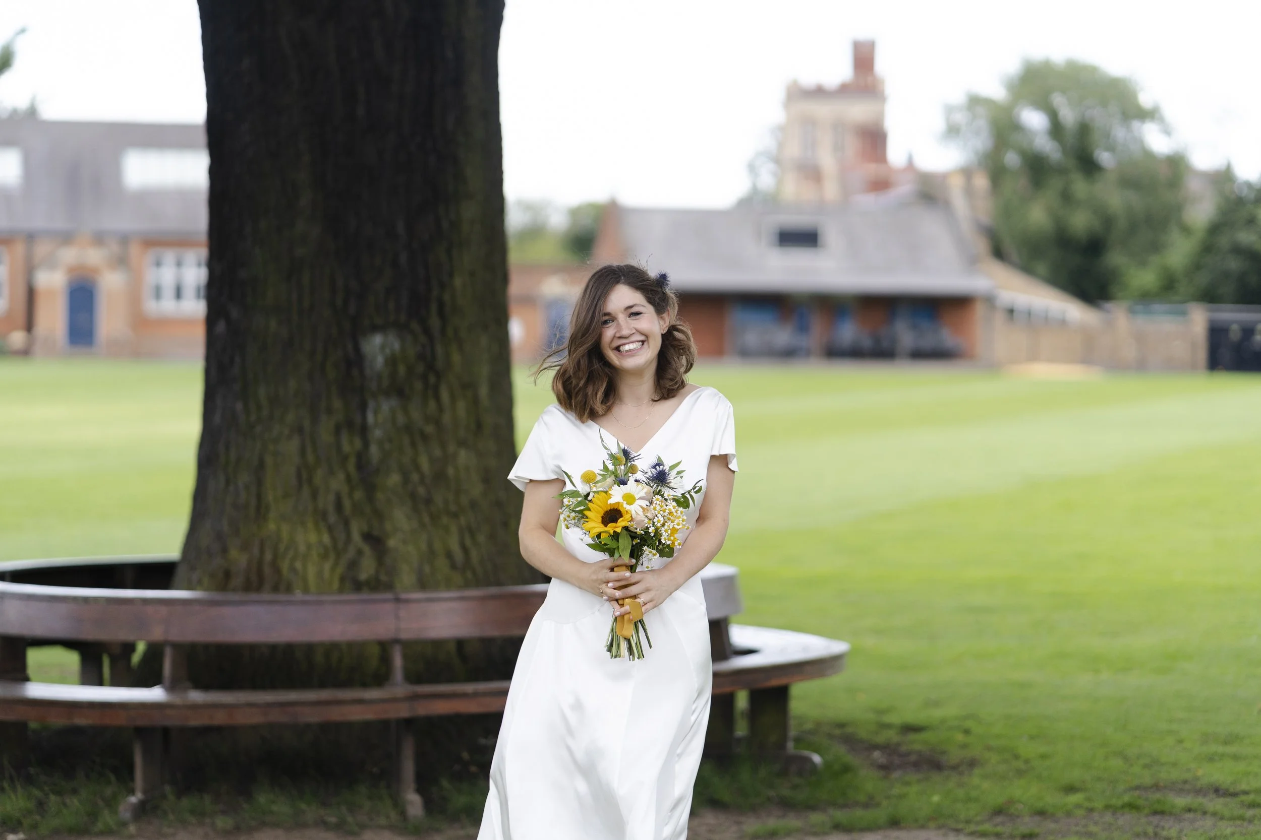 Bride standing next to a tree holding her bouquet and smiling at the camera at a Highgate, London Wedding.