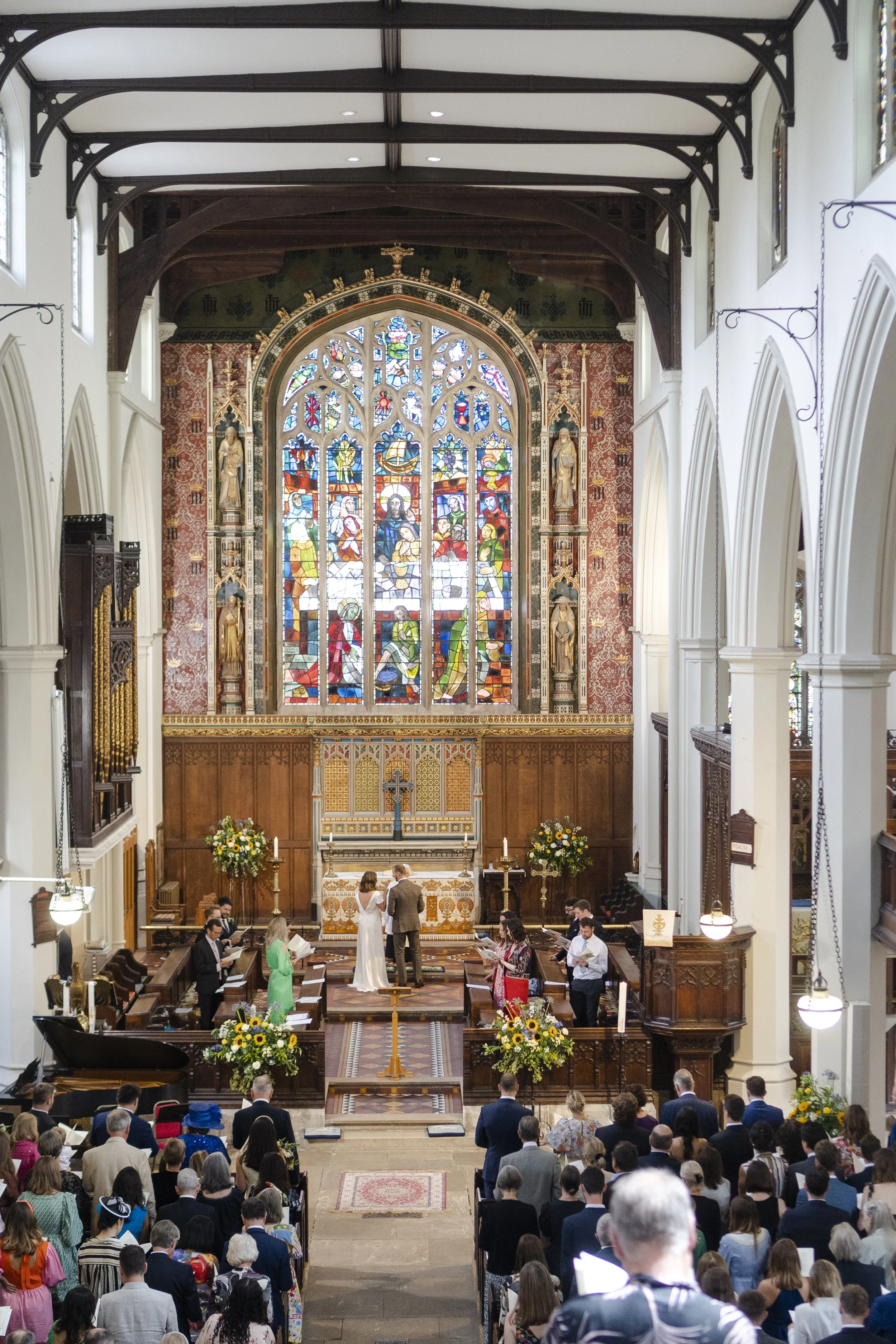 Image taken from the mezzanine of St Michael's Church of the Wedding couple at the top of altar with the main Stained Glass window in full view at a Highgate, London Wedding