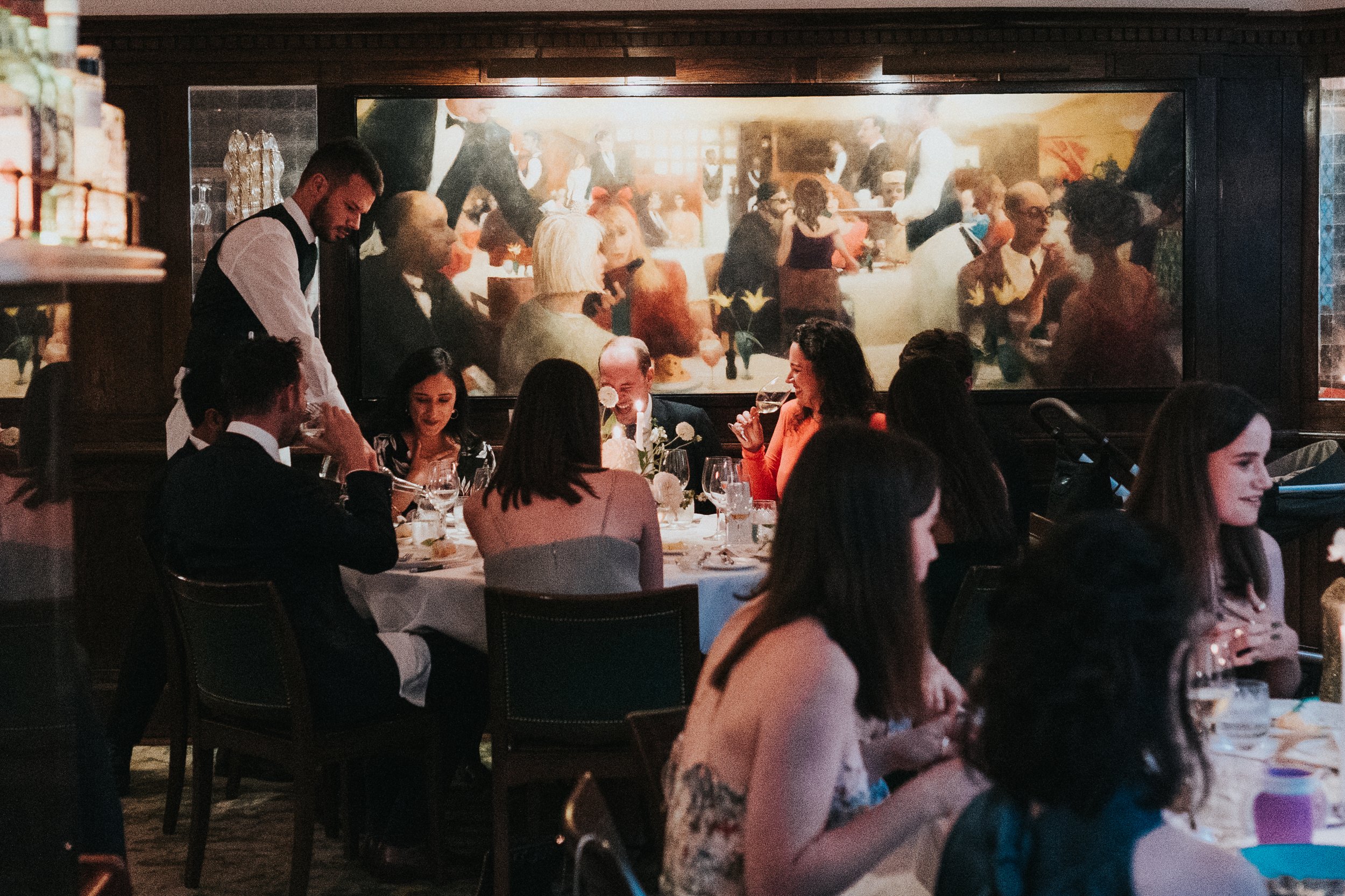Waiter pouring wine at a wedding reception dinner at The Ivy at a Old Marylebone Town Hall Wedding.