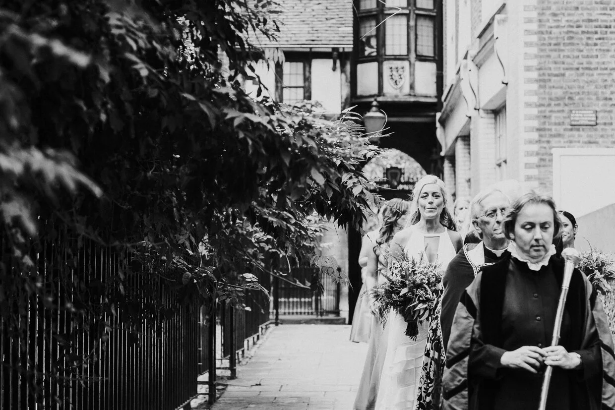 The Verger standing at the front of the procession of the Bride and her bridal party at St Bartholomew the Great church at a City of London Wedding.