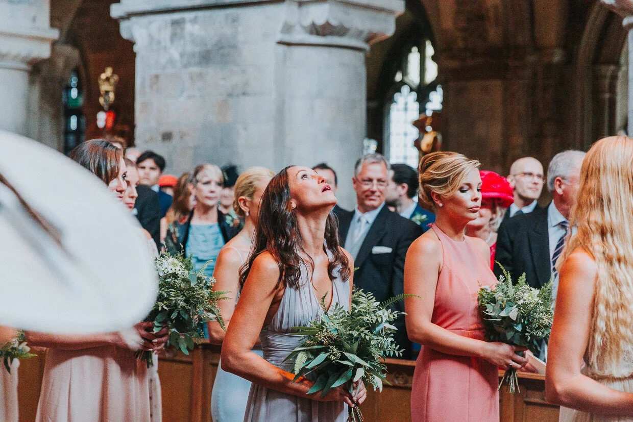 The procession of the Bridal Party walking down the aisle at St Bartholomew the Great church, Smithfield, with one bridesmaids looking up for a City of London Wedding.