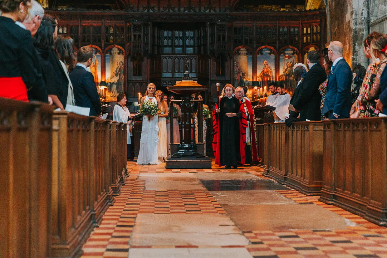 The Bride and the Verger standing at the front of the procession at the back of St Bartholomew the Great church, Smithfield, waiting to walk down the aisle for a City of London Wedding