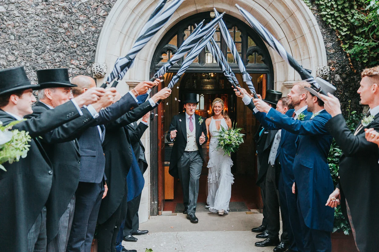 Groomsmen making a guard of honour outside St Bartholomew the Great church, Smithfield, before the wedding couple exits the church at a City of London Wedding.