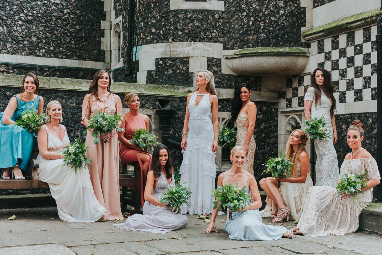 A striking image of the Bride standing and posing with her bridal party either standing or sitting posing like a fashion magazine front cover in the courtyard of St Bartholomew the Great church, Smithfield for a City of London Wedding Photography.