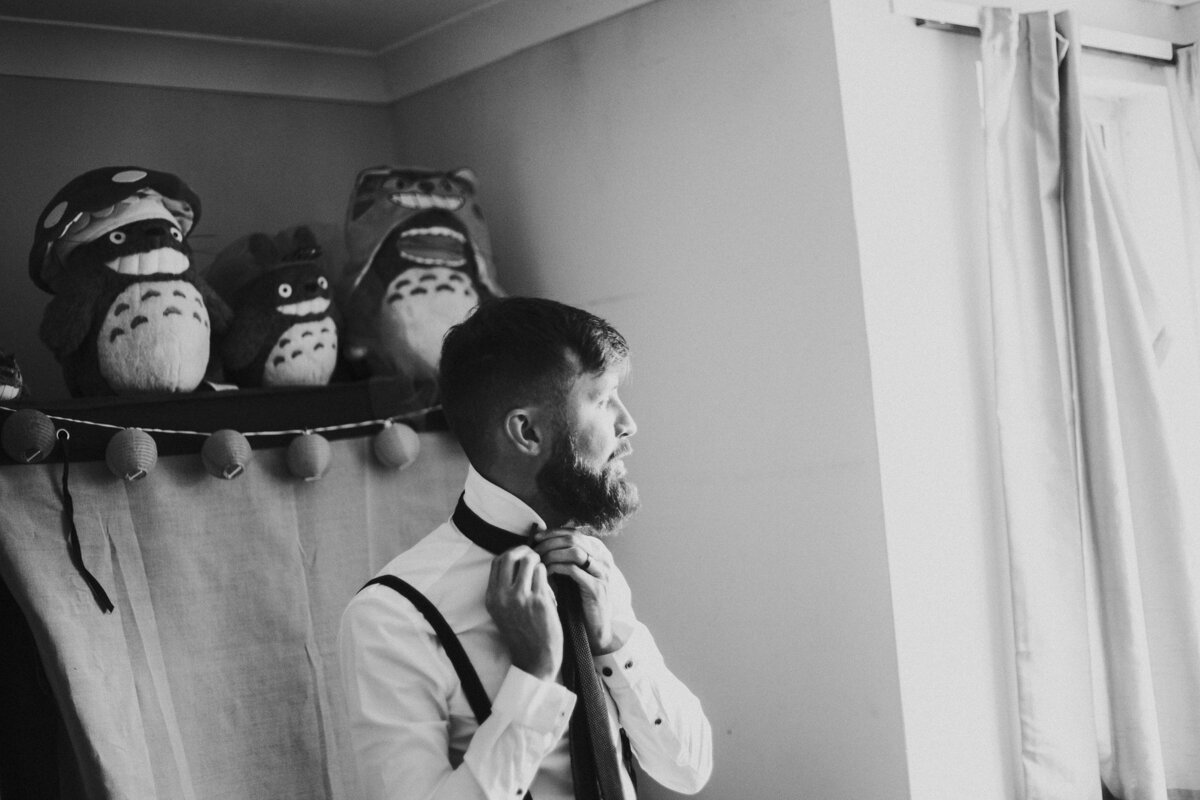 Groom looking out of the window while doing his tie at a London Wedding