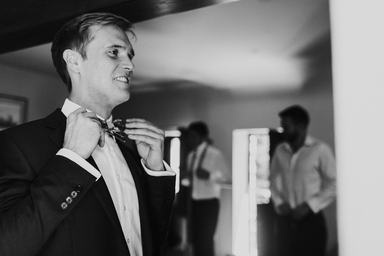 Groom looking in the mirror smiling while rearranging  his bow-tie