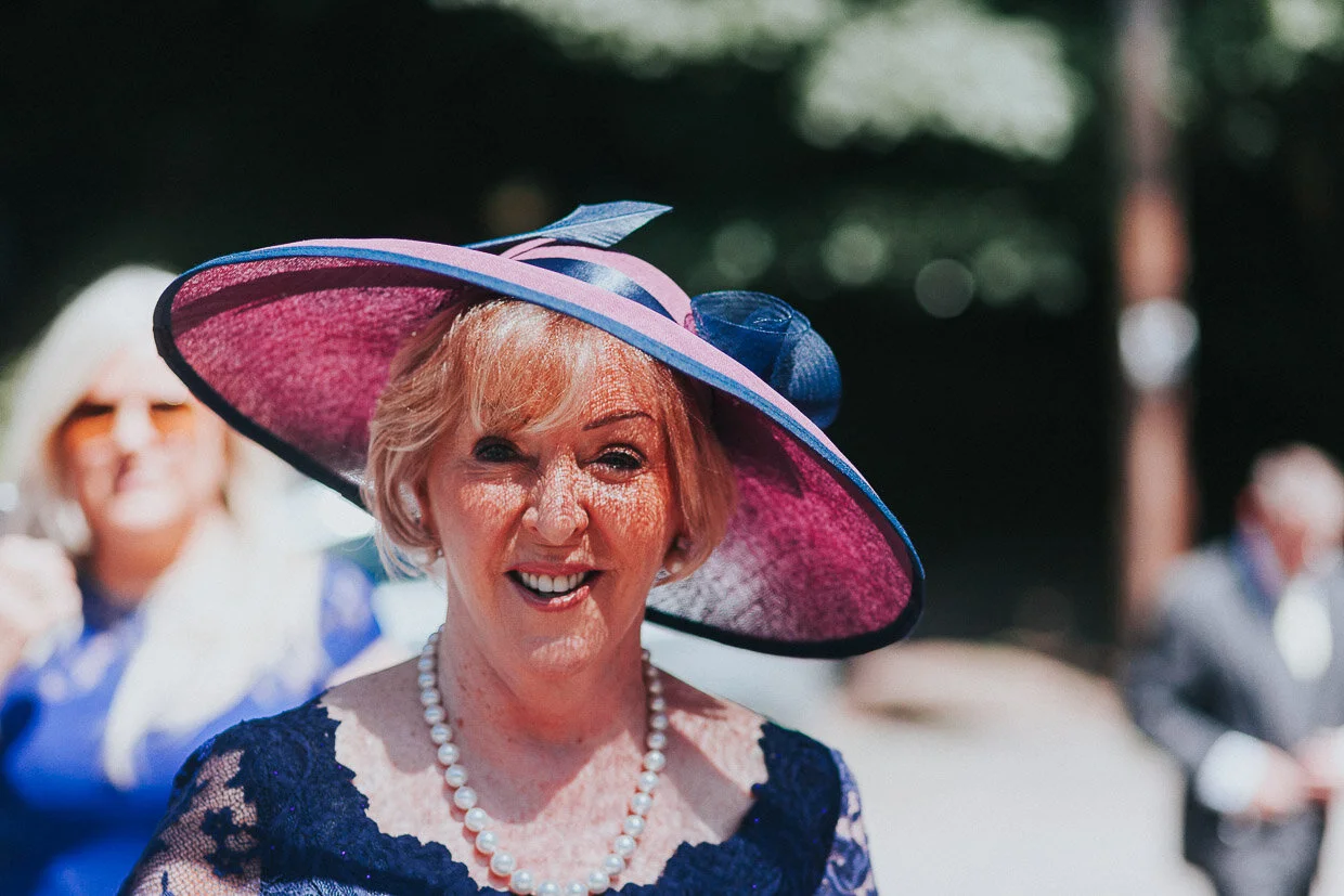 Bride's mother outside church with large hat smiling at the camera on the Ballynatray Estate for a Cork Wedding