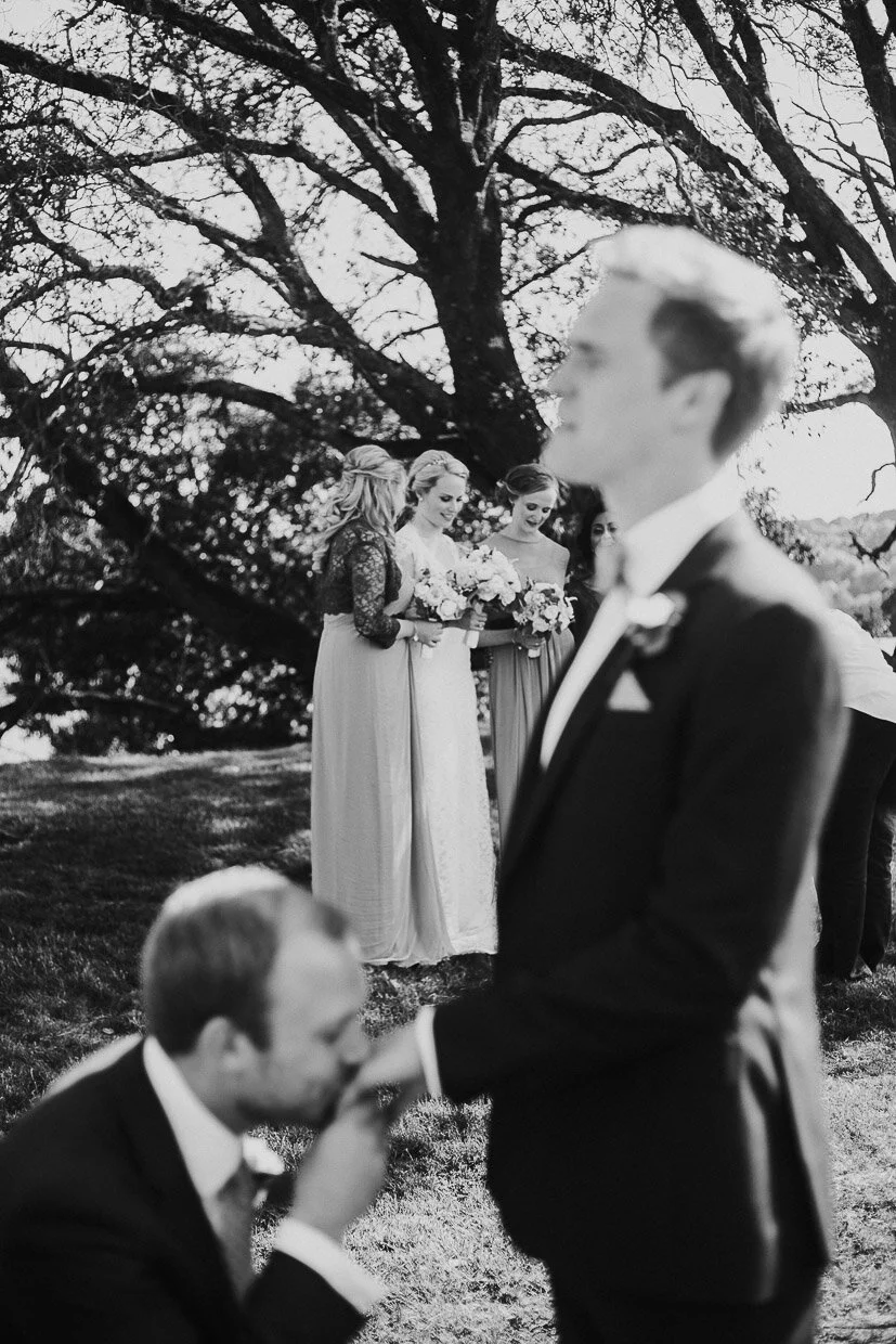 Groomsmen jokely on one knee kissing grooms hand with bridal party in the background on the Ballynatray Estate for a Cork Wedding