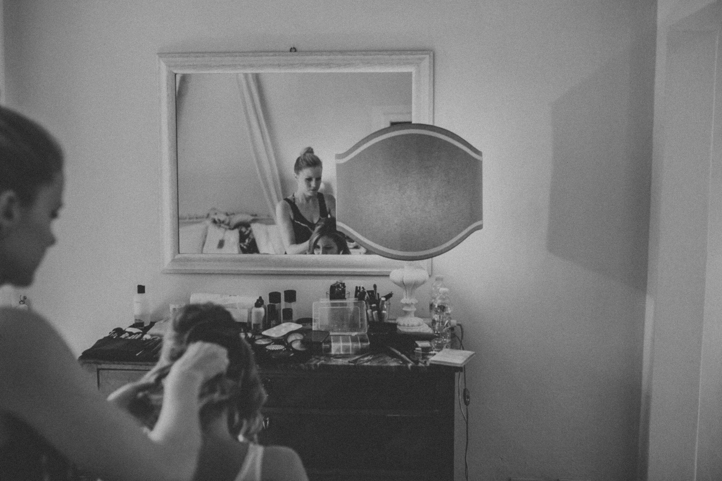 A International Bride sitting in make-up chair getting her hair styles with her reflection in a mirror at a Tuscany Wedding.