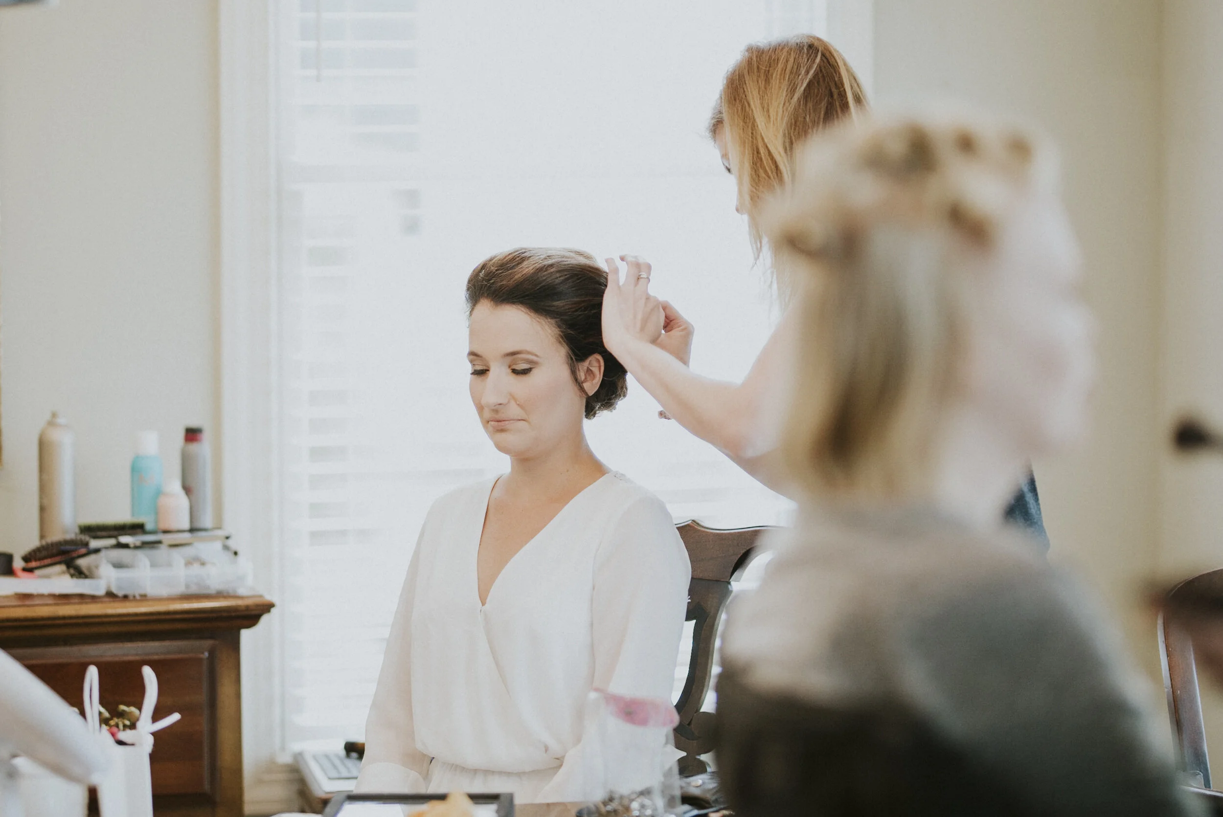 Bride getting her hair done while sitting down with her eyes closed at a Destination Wedding in Rayleigh, North Carolina, USA