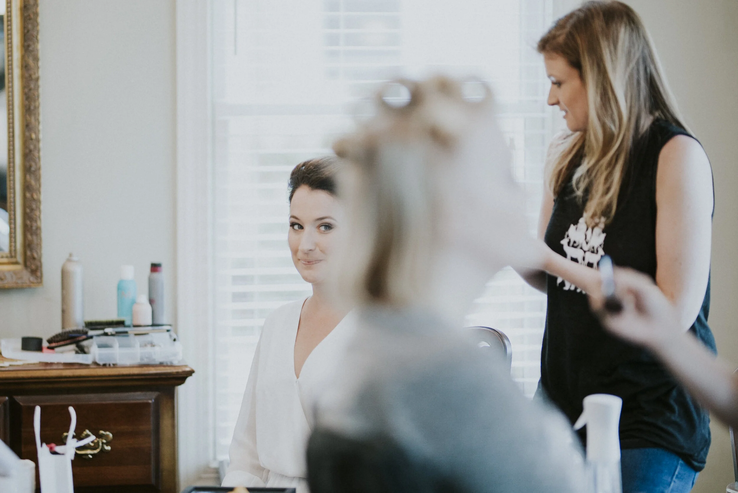A International Bride sitting in the make-up chair looking at her bridesmaids who is blurred in forefront at a North Carolina Wedding