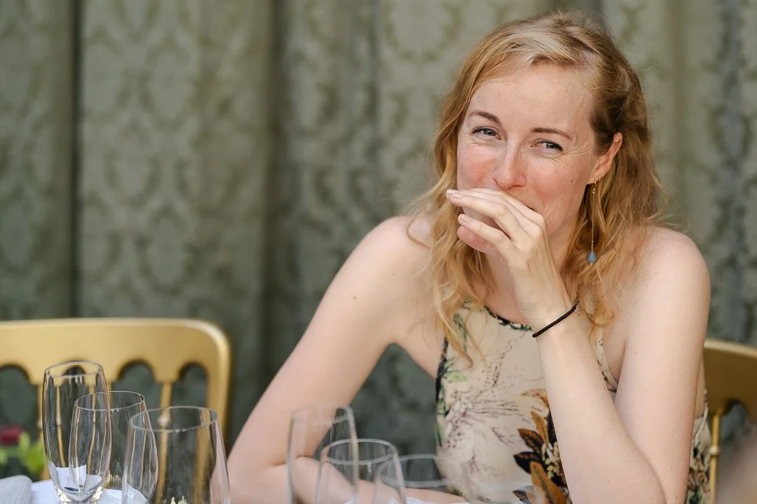 A guest covers her mouth while smiling and laughing at the dinner table at a Hampton Court House Wedding.