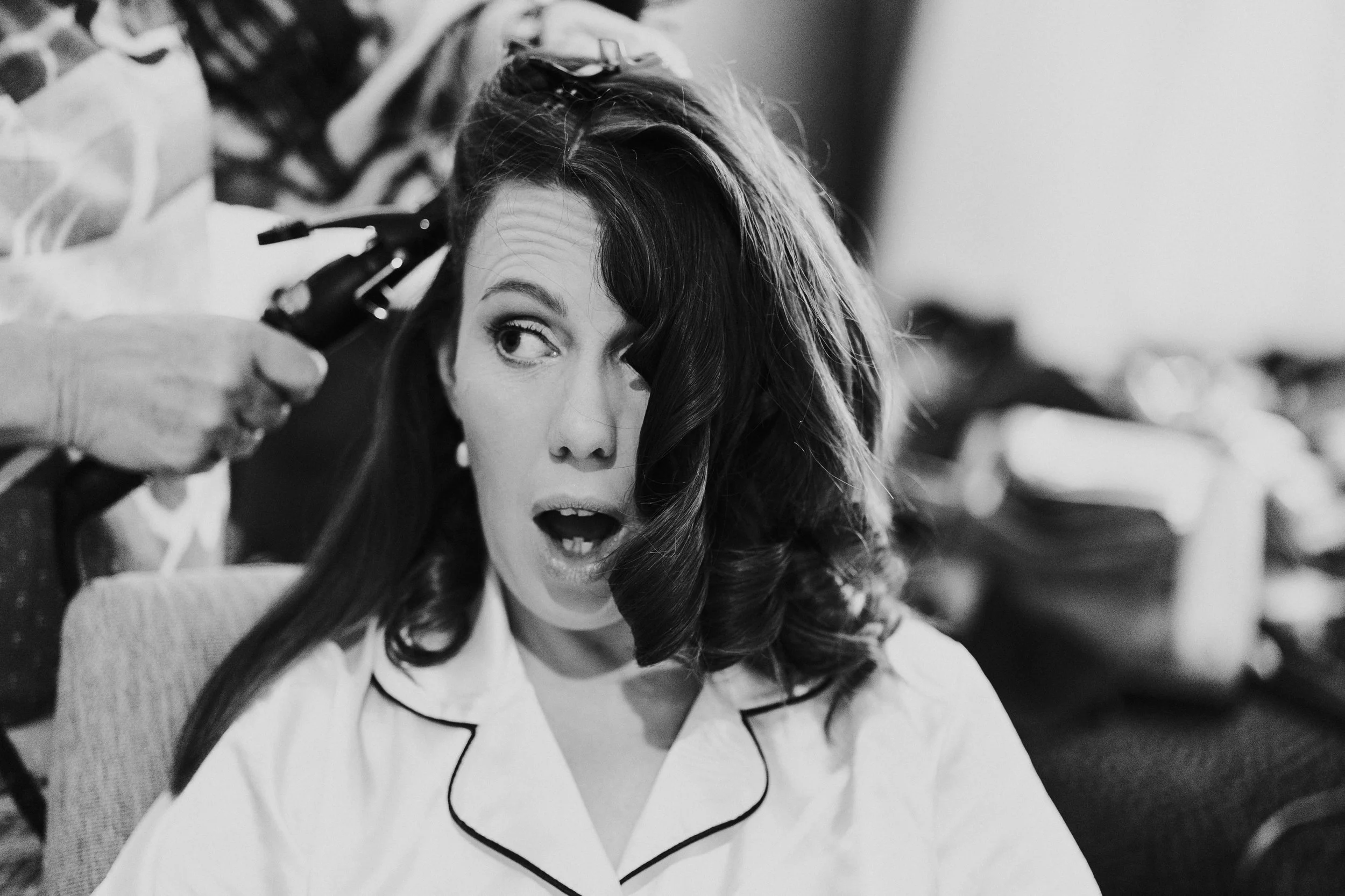 Bride who is having her hair curled with heated togs with a shocked look and looking to the side at Benson Village Oxfordshire Wedding