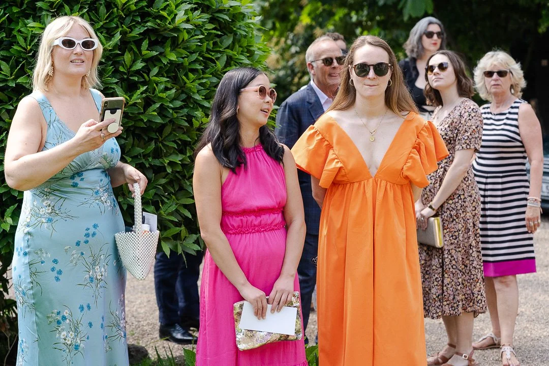 Guests in colourful dresses standing together talking to each other at a Hampton Court House Wedding.