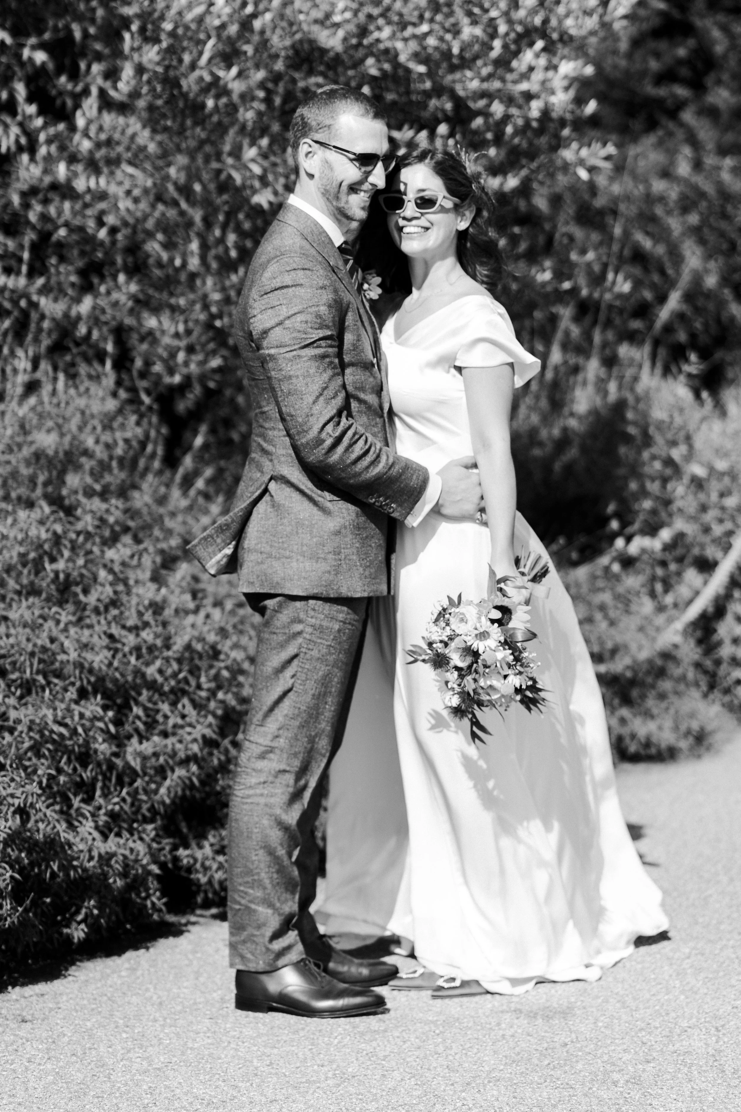 Wedding couple posing for portraits wearing sunglasses facing each other and smiling at a Highgate, London Wedding.