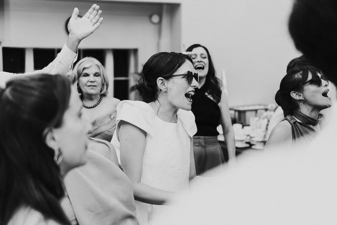 Bride in the middle of the dancefloor wearing heart-shaped sunglasses cheering and dancing at a Hampton Court House Wedding