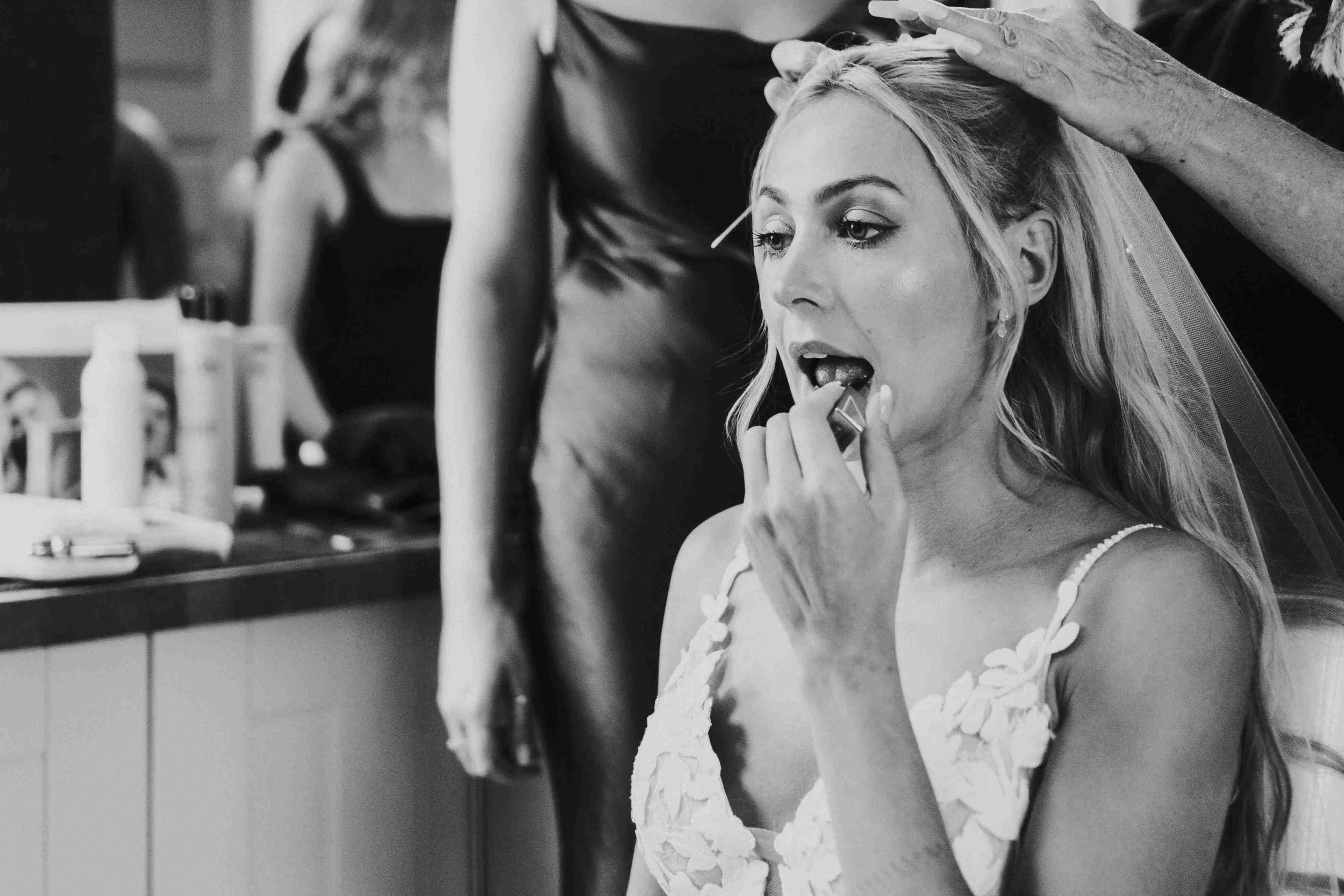 Bride applying lipstick while her veil is being attached before her Halfmoon Farm Wedding in Rutland
