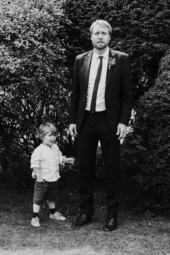 Guests standing with a bit of a look of disbelief with a small child smiling and standing next to him at a Hampton Court House Wedding.