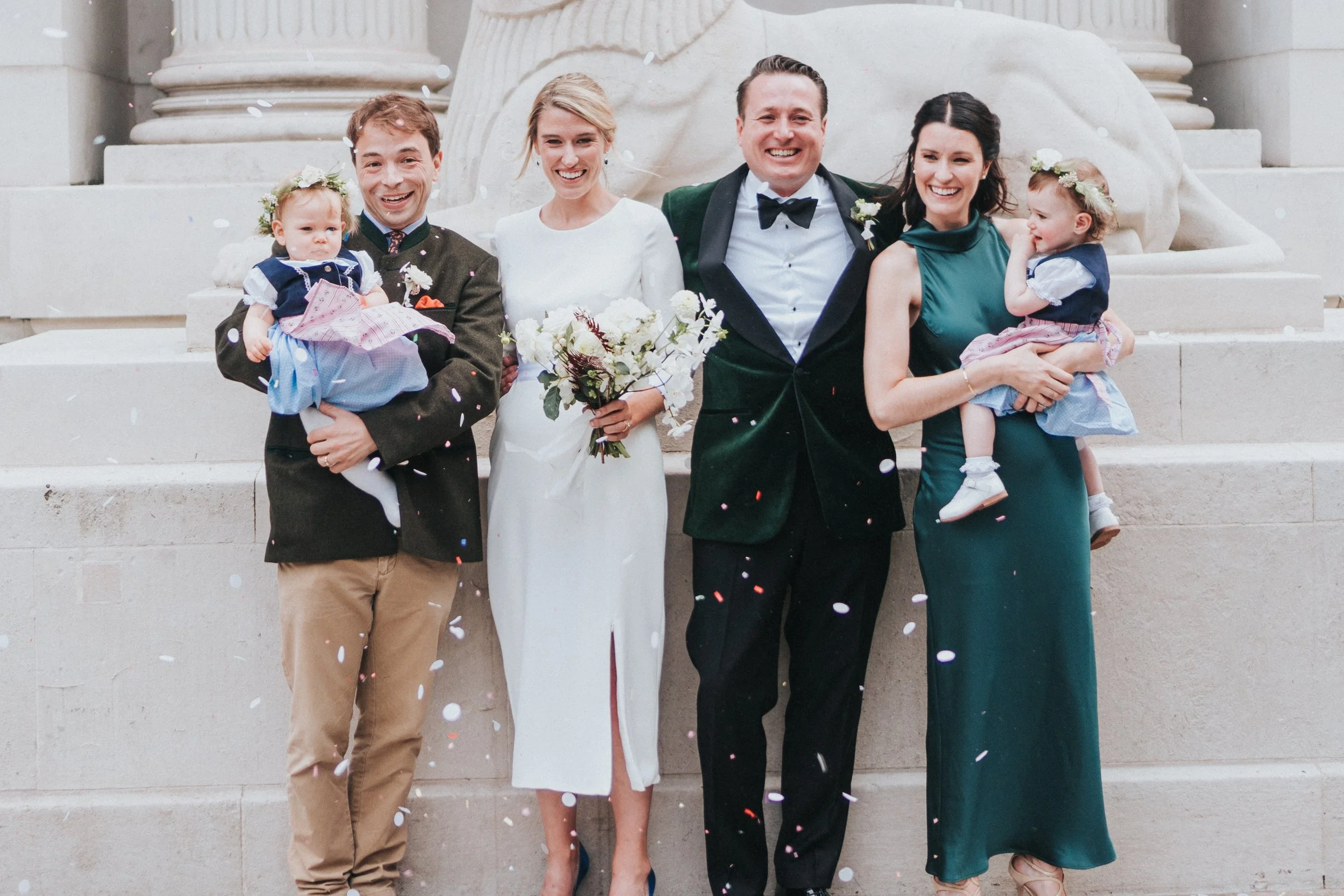 Wedding couple posing with guests and their young children in front of the iconic Lion with confetti blowing past them at a Old Marylebone Town Hall Wedding