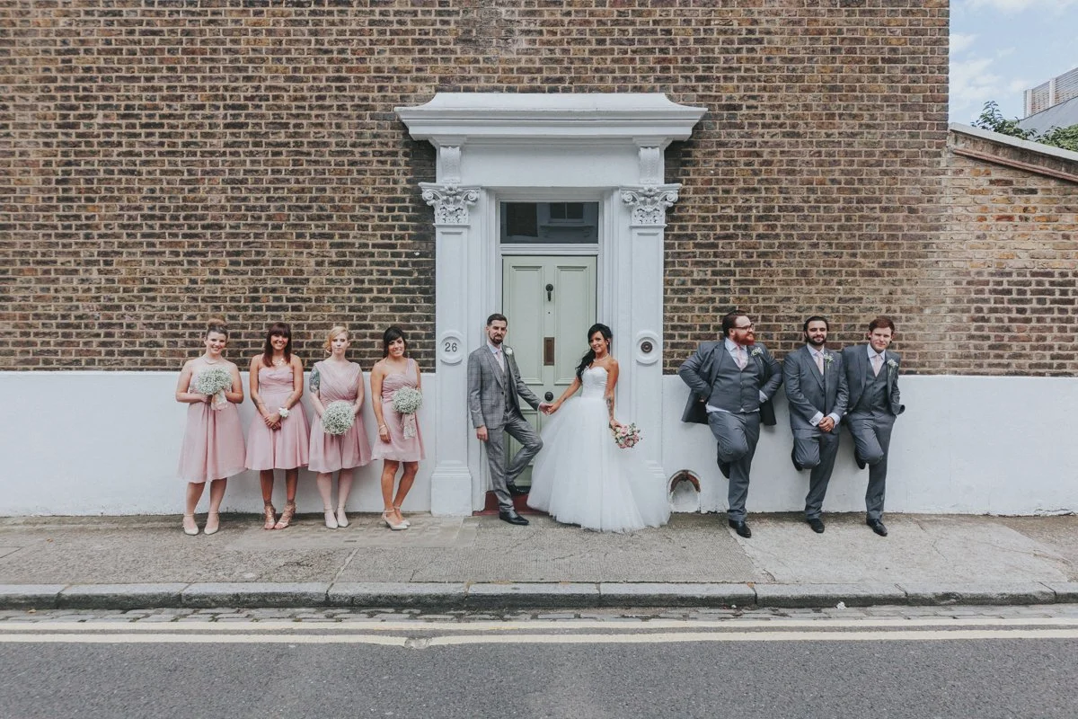 Bridal Party posing and leaning against a wall while the Bride & Groom pose together against a front door near Islington Town Hall Wedding Venue
