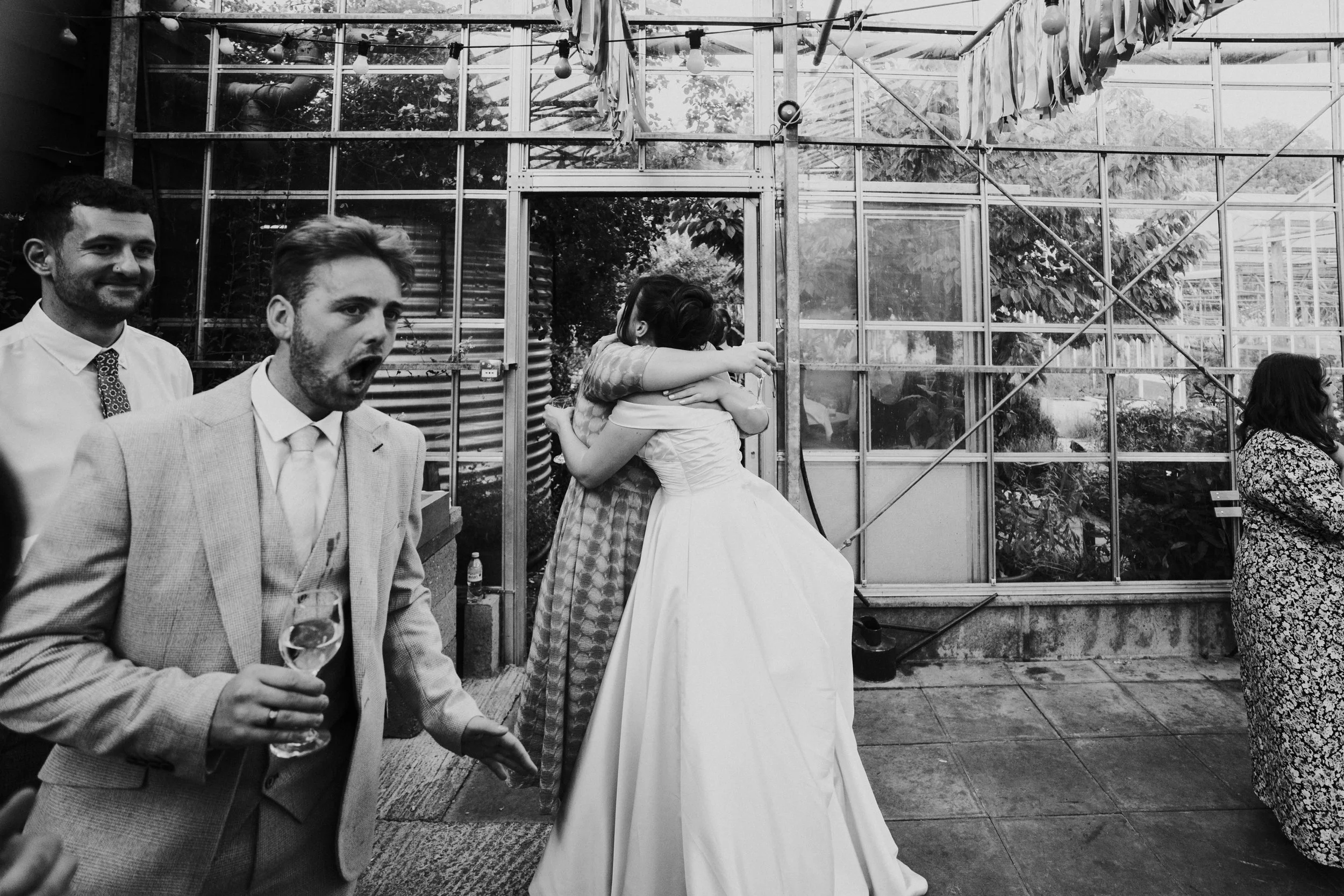 Bride hugging a guest while another guest walks past with a shock look on his face at a Worton Kitchen Garden, Oxfordshire Wedding.