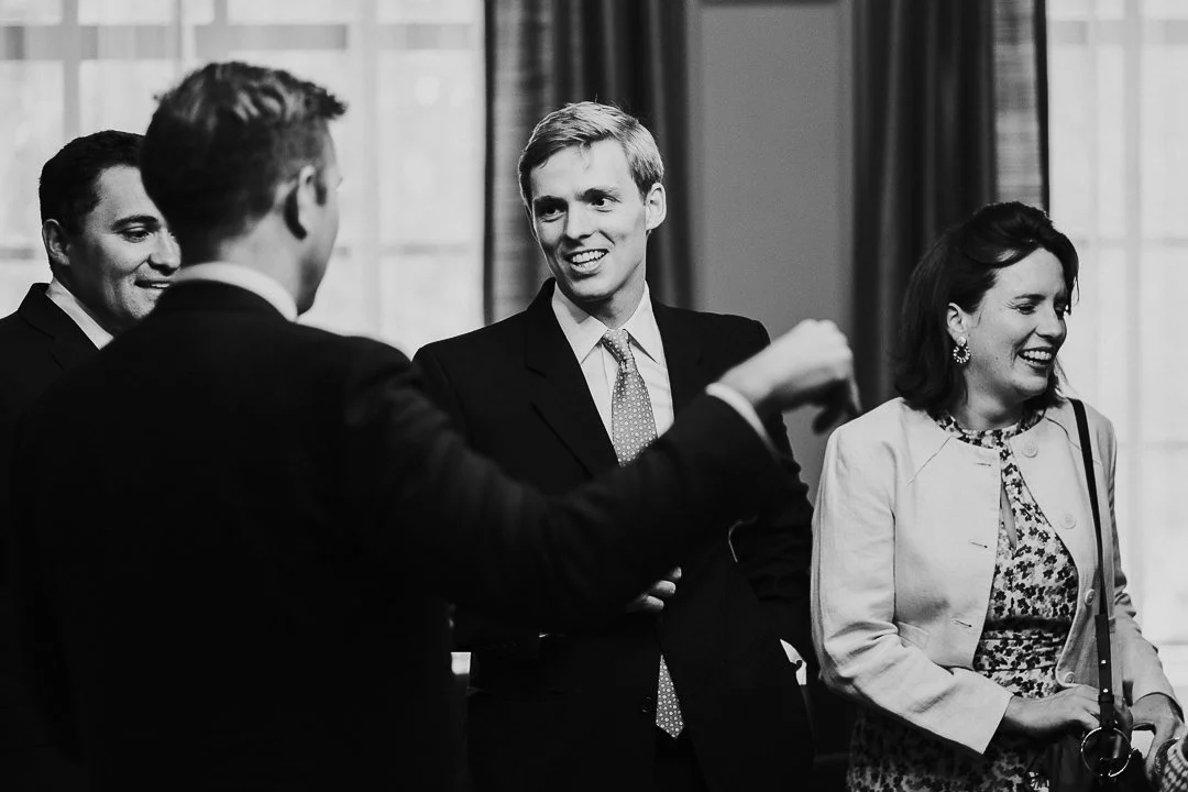 Male guests talking while a female guest is laughing with someone out of shot in the ceremony room at the Old Marylebone Town Hall Wedding