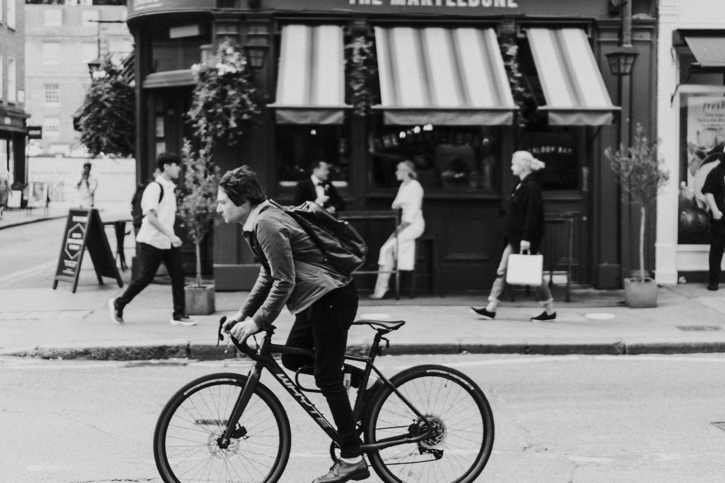 Cyclist in foreground passing the Wedding couple sitting outside The Marylebone before a Old Marylebone Town Hall Wedding