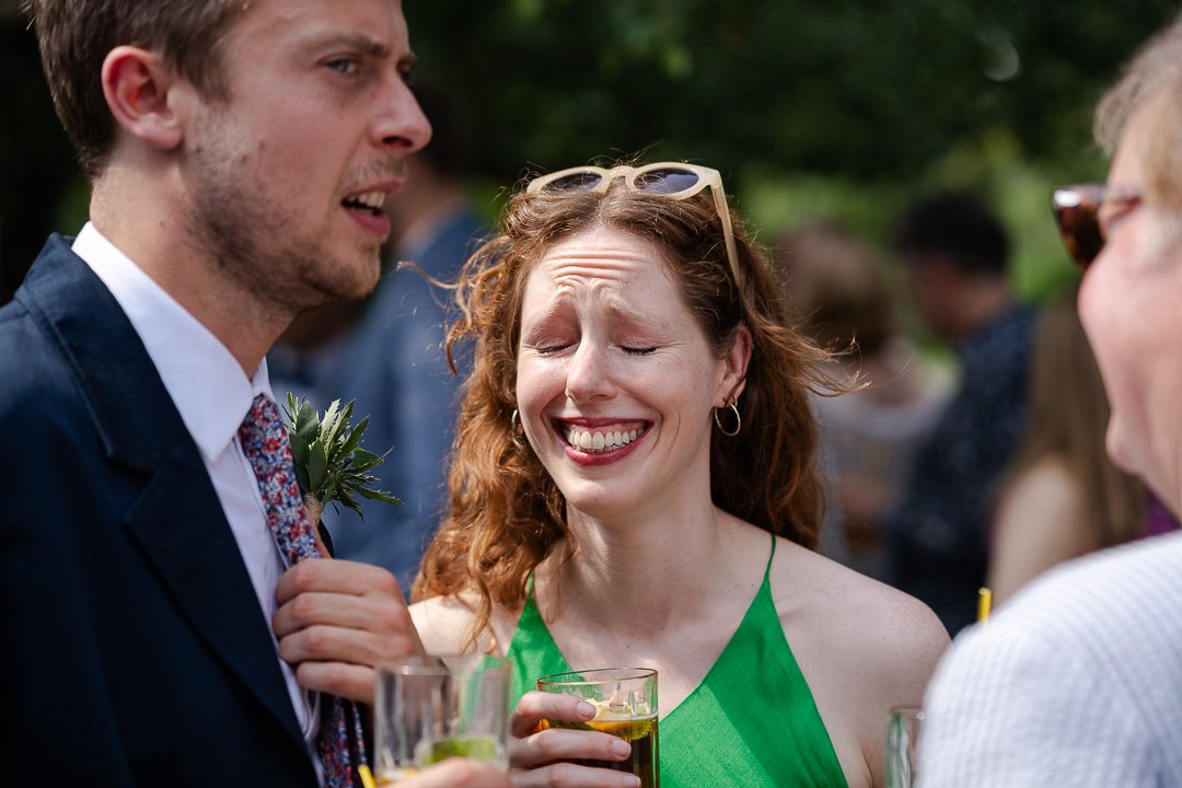 One guest in a green dress and holding a glass with Pimms, laughing while another guest looks into the distance at a Hampton Court House Wedding.