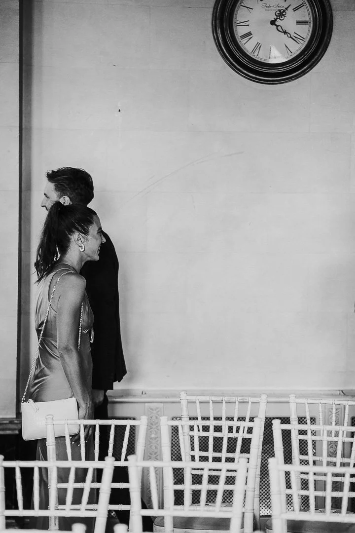 Black & White image of a guest and the Grooms passing each other both looking forward and smiling while walking past each other at a Hampton Court House Wedding.