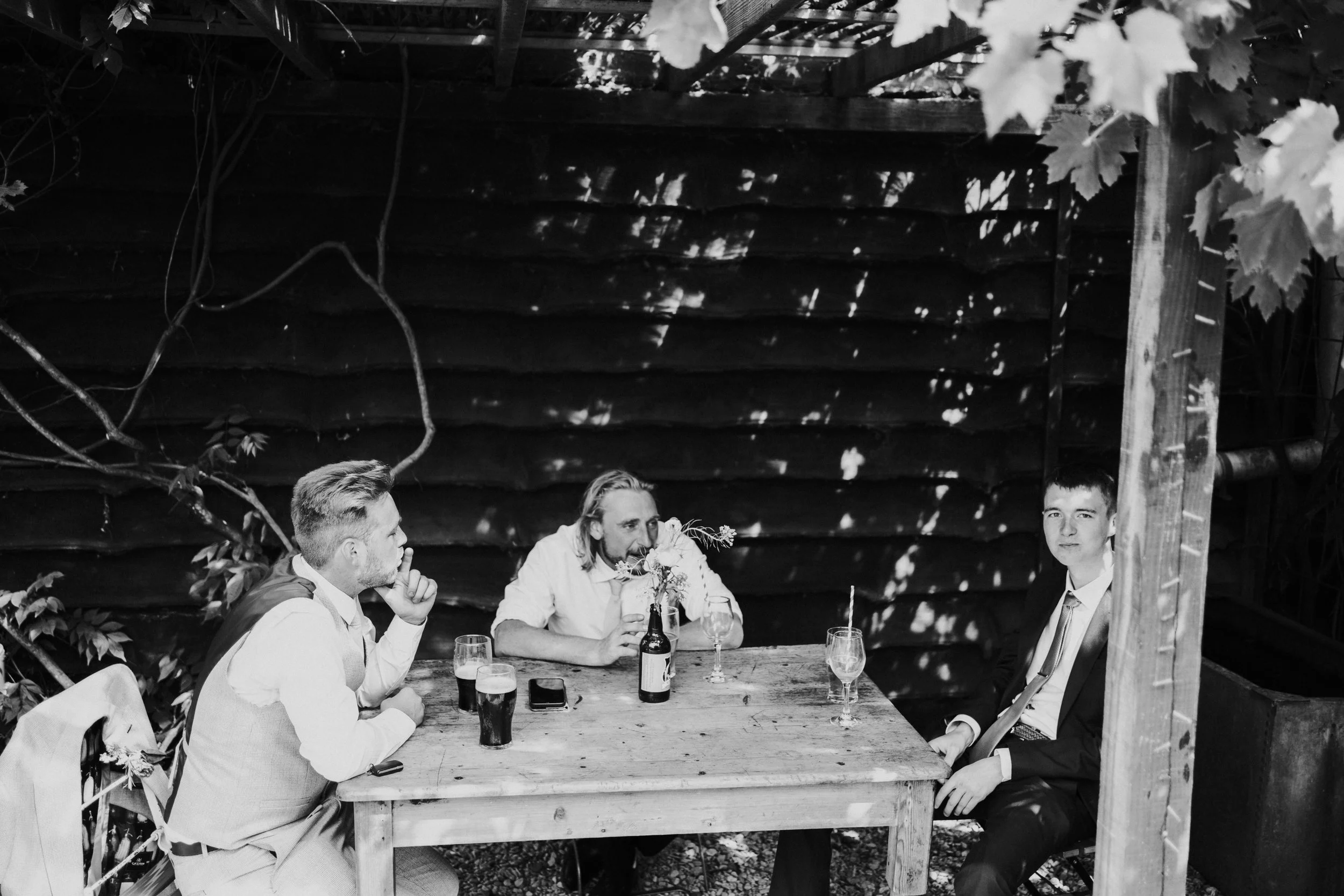Wedding guests sitting at a table chatting and smoking at a Worton Kitchen Garden, Oxfordshire Wedding.
