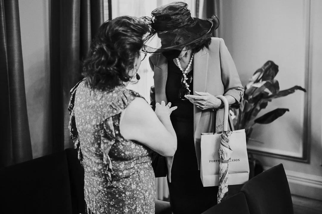 Guest with large hat covering her face while she speaks to another guest at the Old London Marylebone Town Hall Wedding