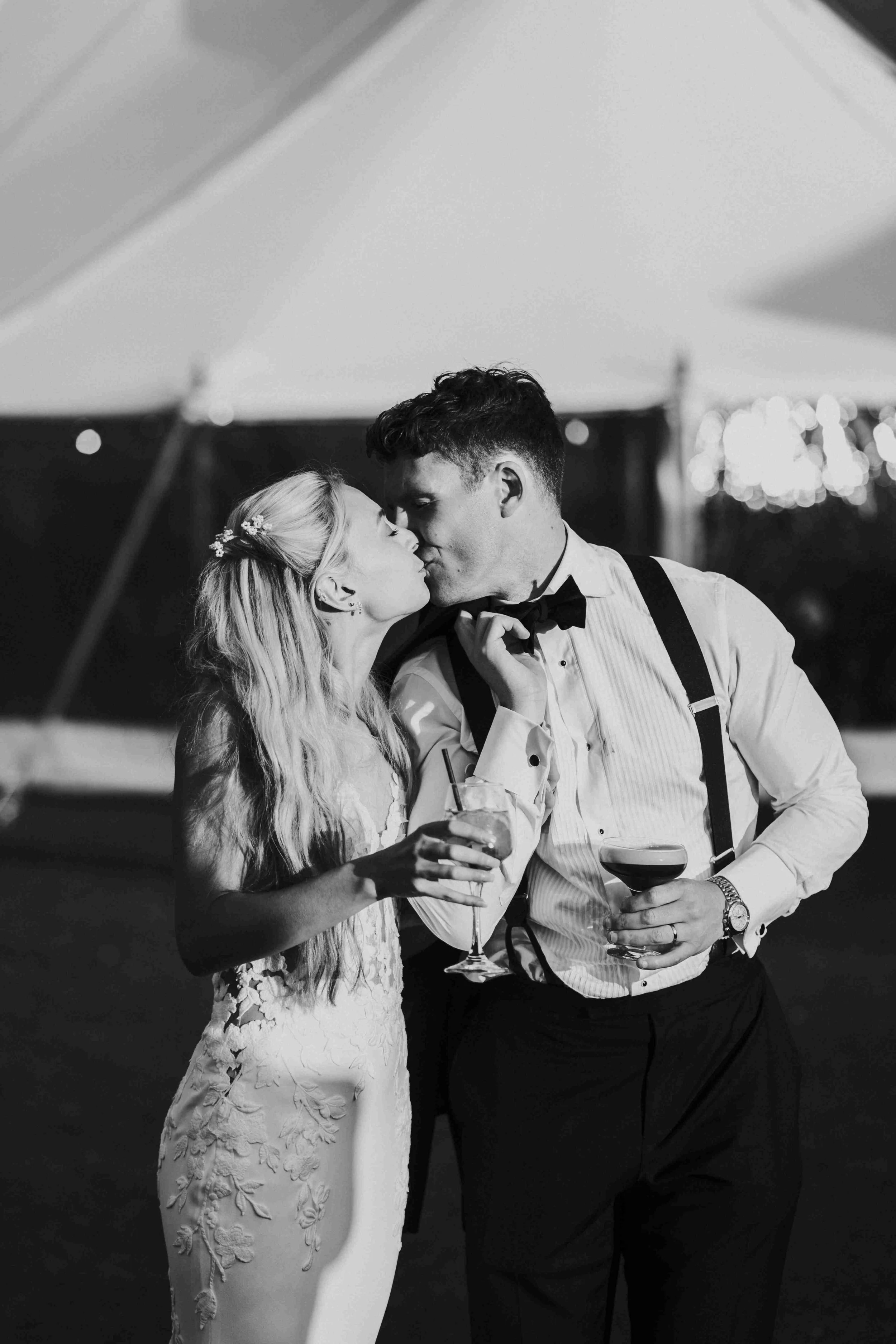 Couple outside the Wedding Reception Marquee kissing while holding cocktails at the Halfmoon Farm Wedding in Rutland