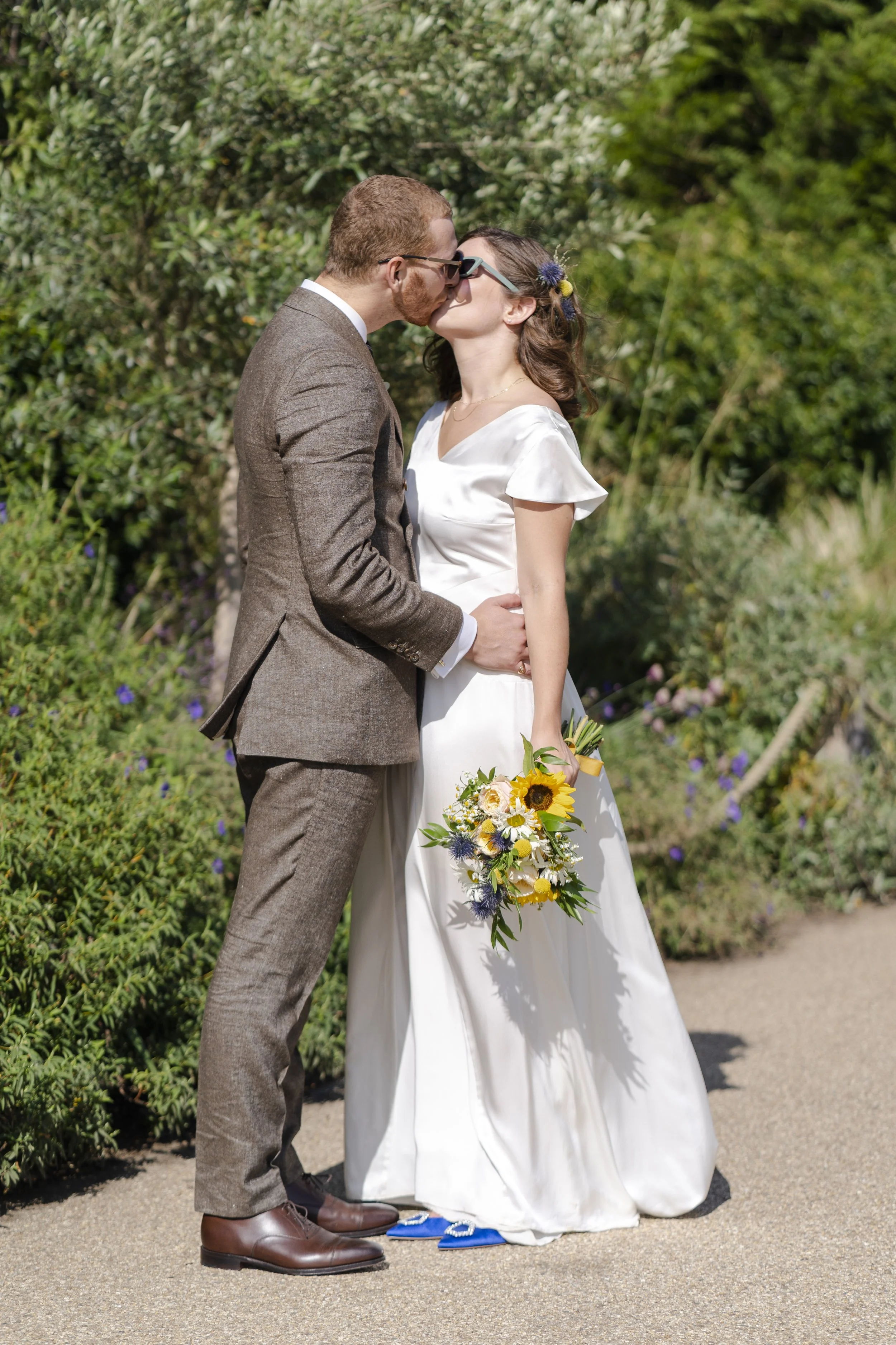 Wedding couple posing for portraits wearing sunglasses standing and kissing at a Highgate, London Wedding.