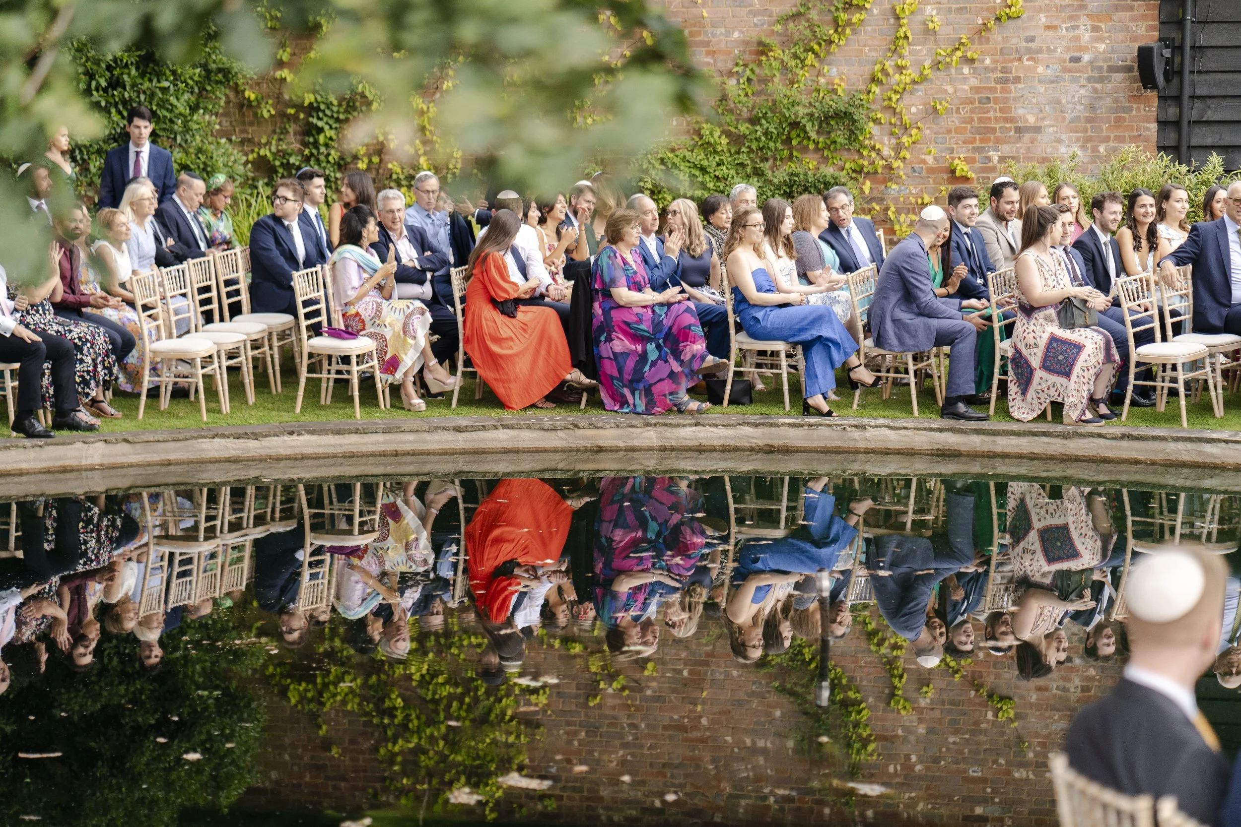 Wedding guest sitting down for the ceremony with the reflection in the pond at a Micklefield Hall Wedding