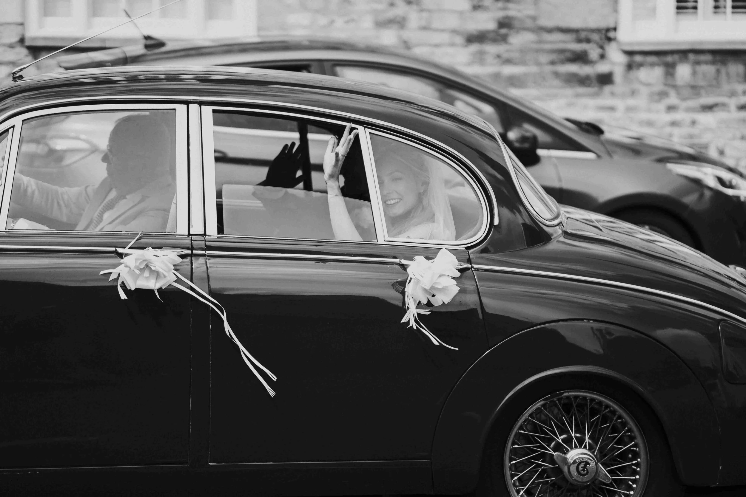 The Couple in the back seat of the wedding car waving before being driven off to the reception at the Halfmoon Farm Wedding in Rutland