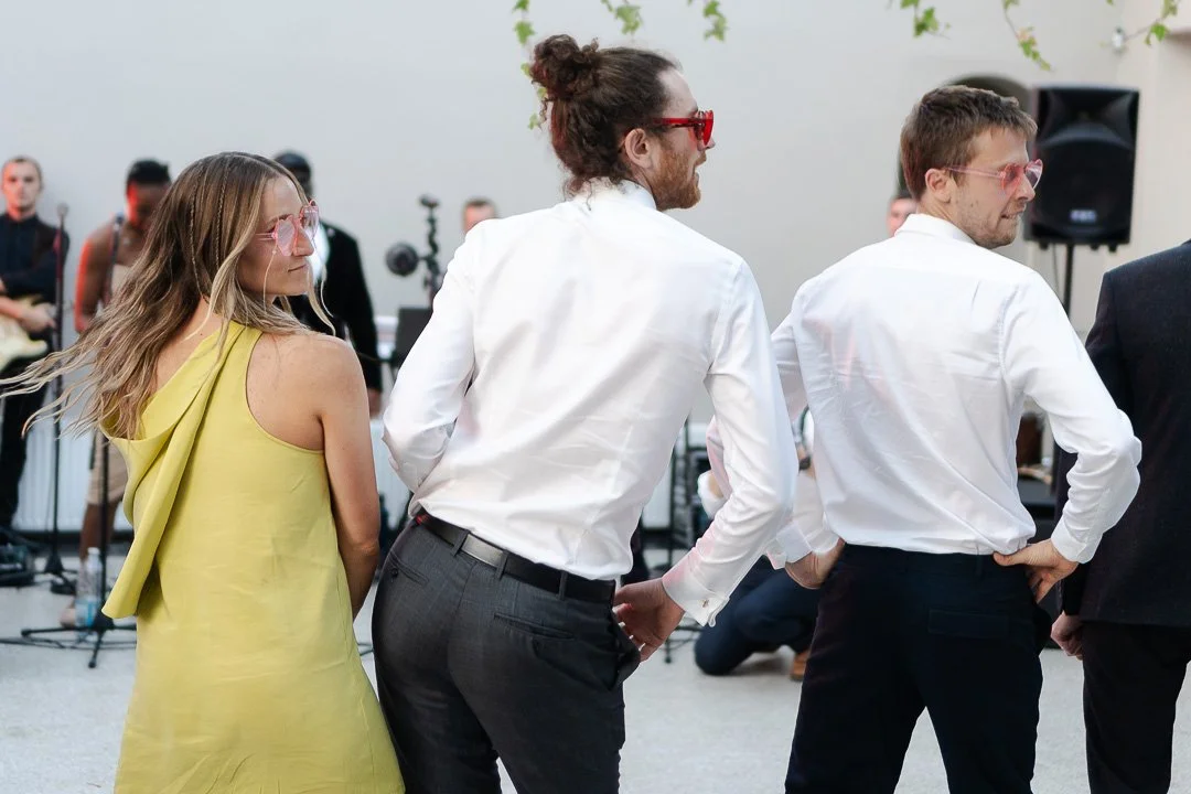 Guests who backs are to the camera performing a dance on the dancefloor wearing heart-shaped sunglasses at a Hampton Court House Wedding.