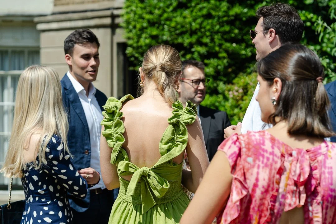 Guests in colorful dresses standing around and chatting with other guests at a Hampton Court House Wedding.