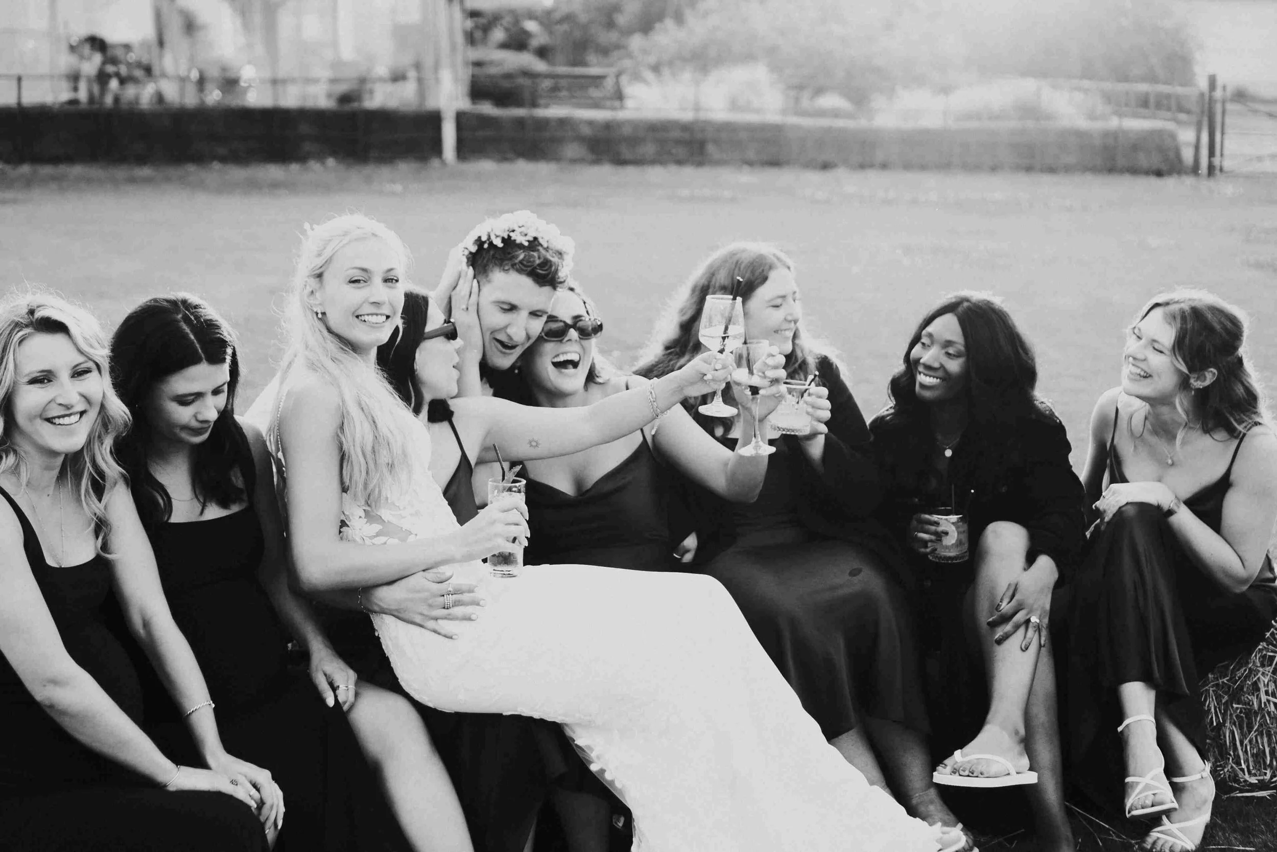 Bride & Groom with guest sitting on Hay Bales with the Groom wearing a flower crown at the Halfmoon Farm Wedding in Rutland