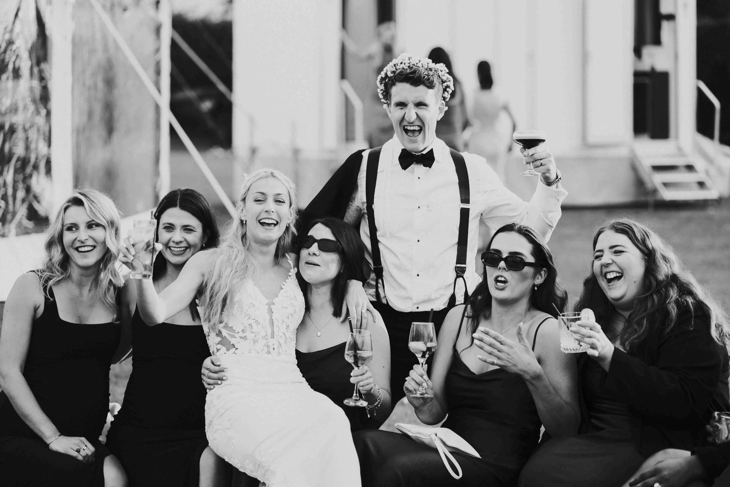 Guests with the Couple sitting on a Hay Bale with the Groom wearing a Flower Crown at the Halfmoon Farm Wedding in Rutland
