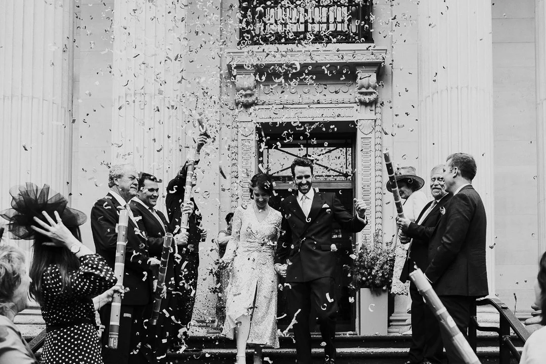 Wedding couple smiling and laughing while walking down the steps while confetti falls down on them at the Old Marylebone Town Hall Wedding.