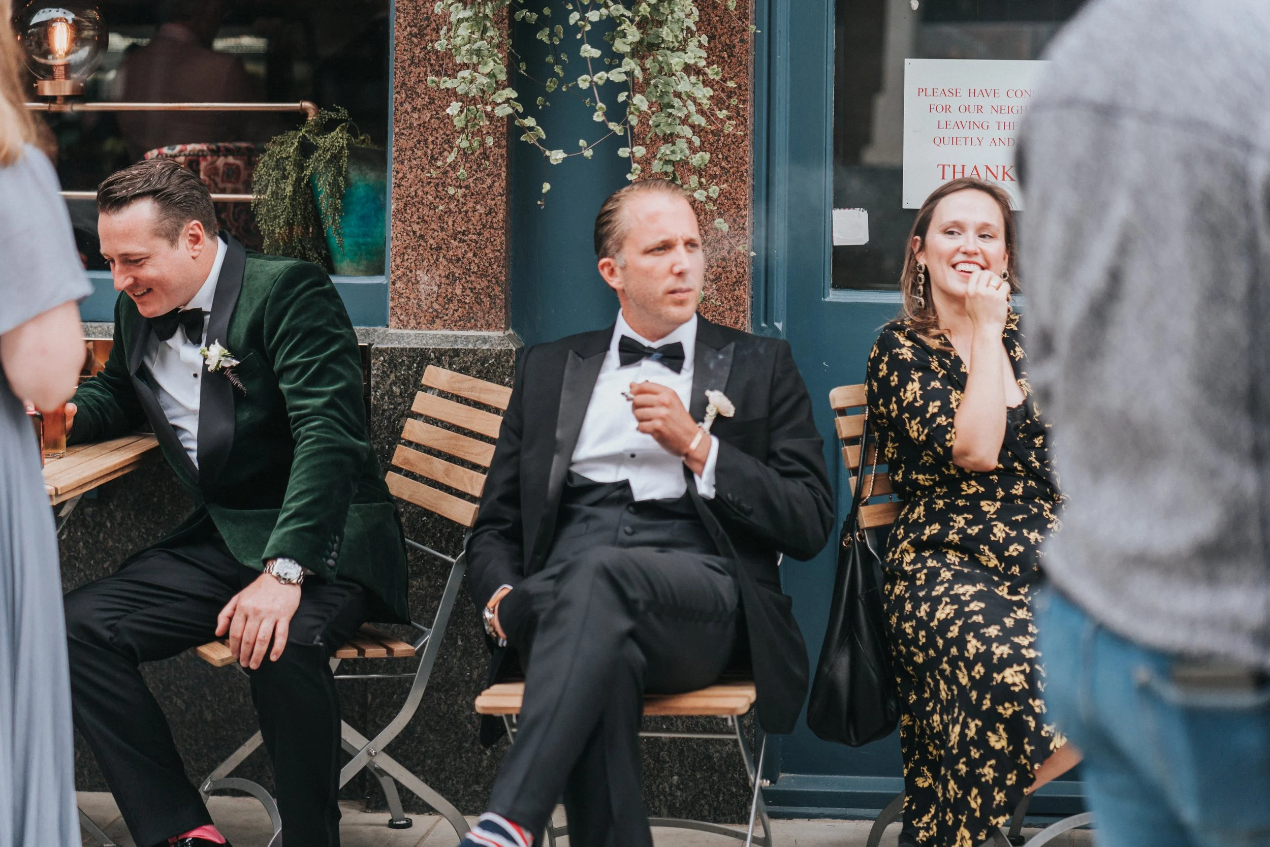 Wedding guests sitting outside a pub with one smoking at a Old Marylebone Town Hall Wedding