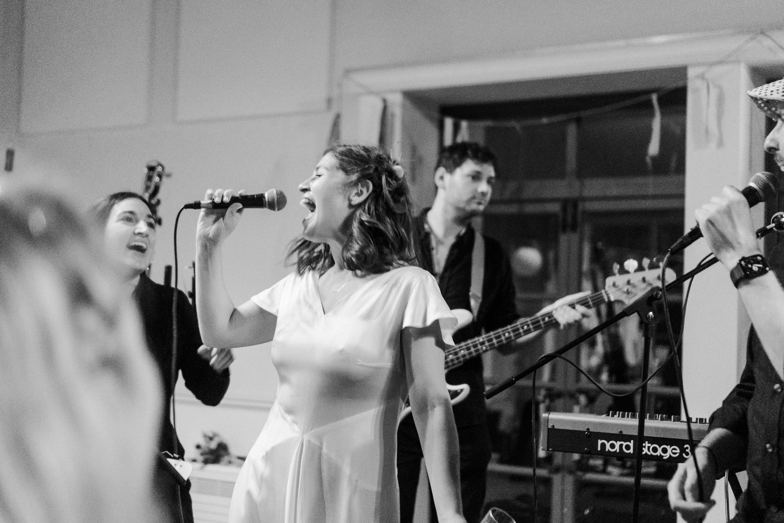 Bride standing on stage singing in front of her guest with the band beside her at a Highgate, London Wedding.