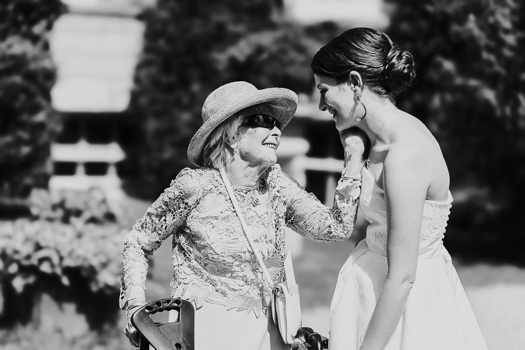 The bride's Grandma embraces the bride with one hand while the bride smiles at her at a Hampton Court House Wedding.