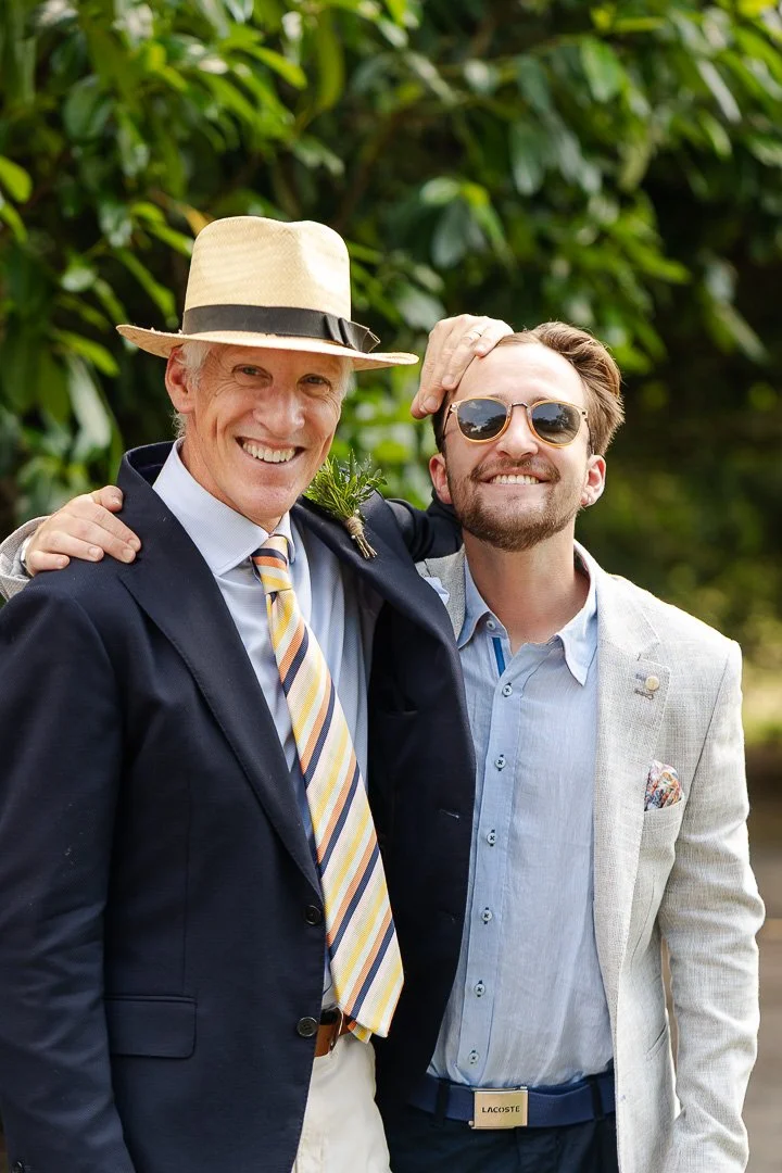 Two Guests posing for the camera, one wearing a panama hat and the other wearing sunglasses both smiling at the camera at a Hampton Court House Wedding.