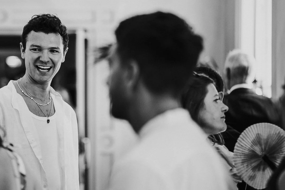 Guest in open top shirt smiling and laughing with another guest  at a Hampton Court House Wedding.