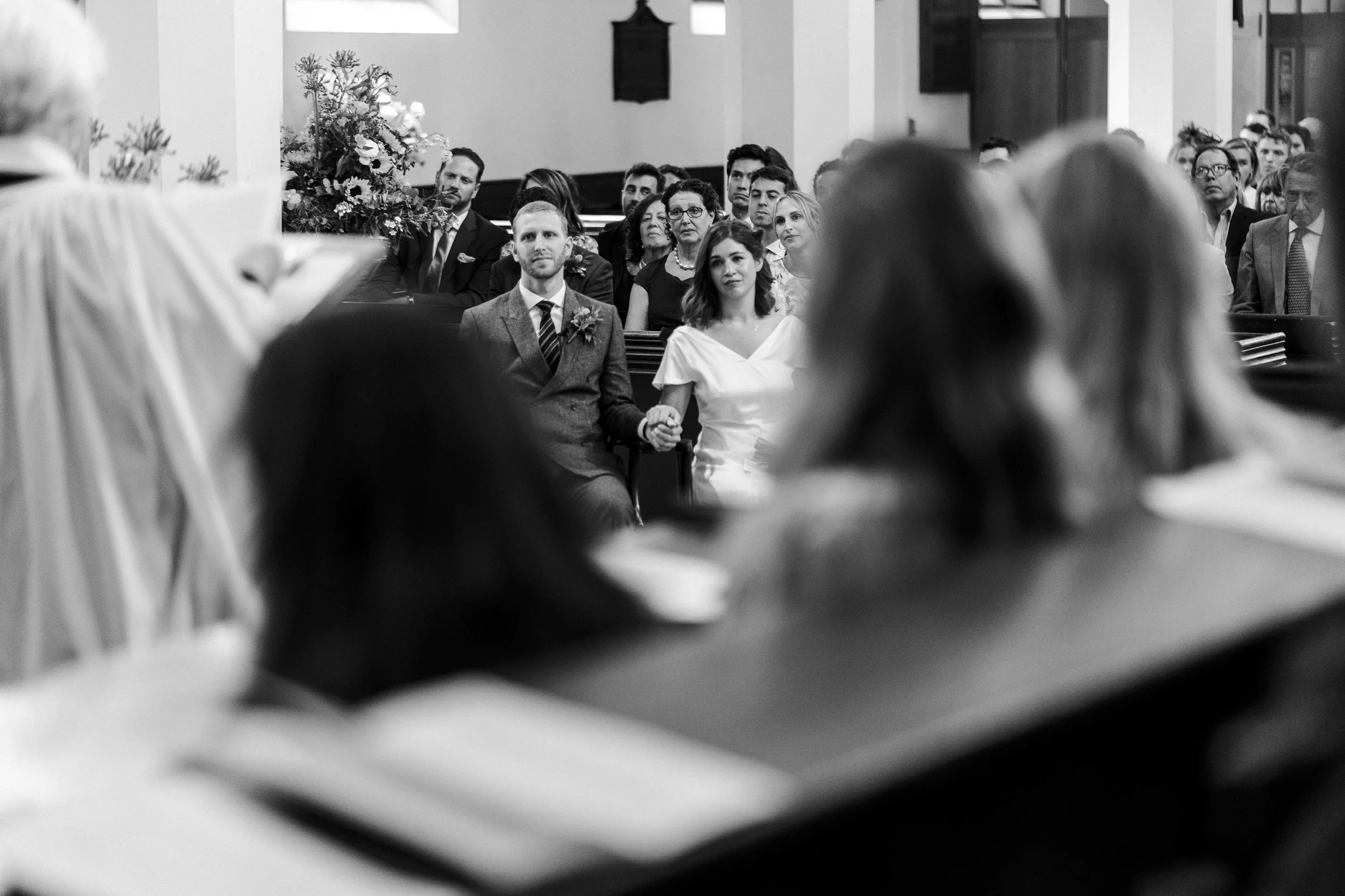 Wedding couple sitting, holding hands and watching the choir perform at St Michael's Church at a Highgate, London Wedding