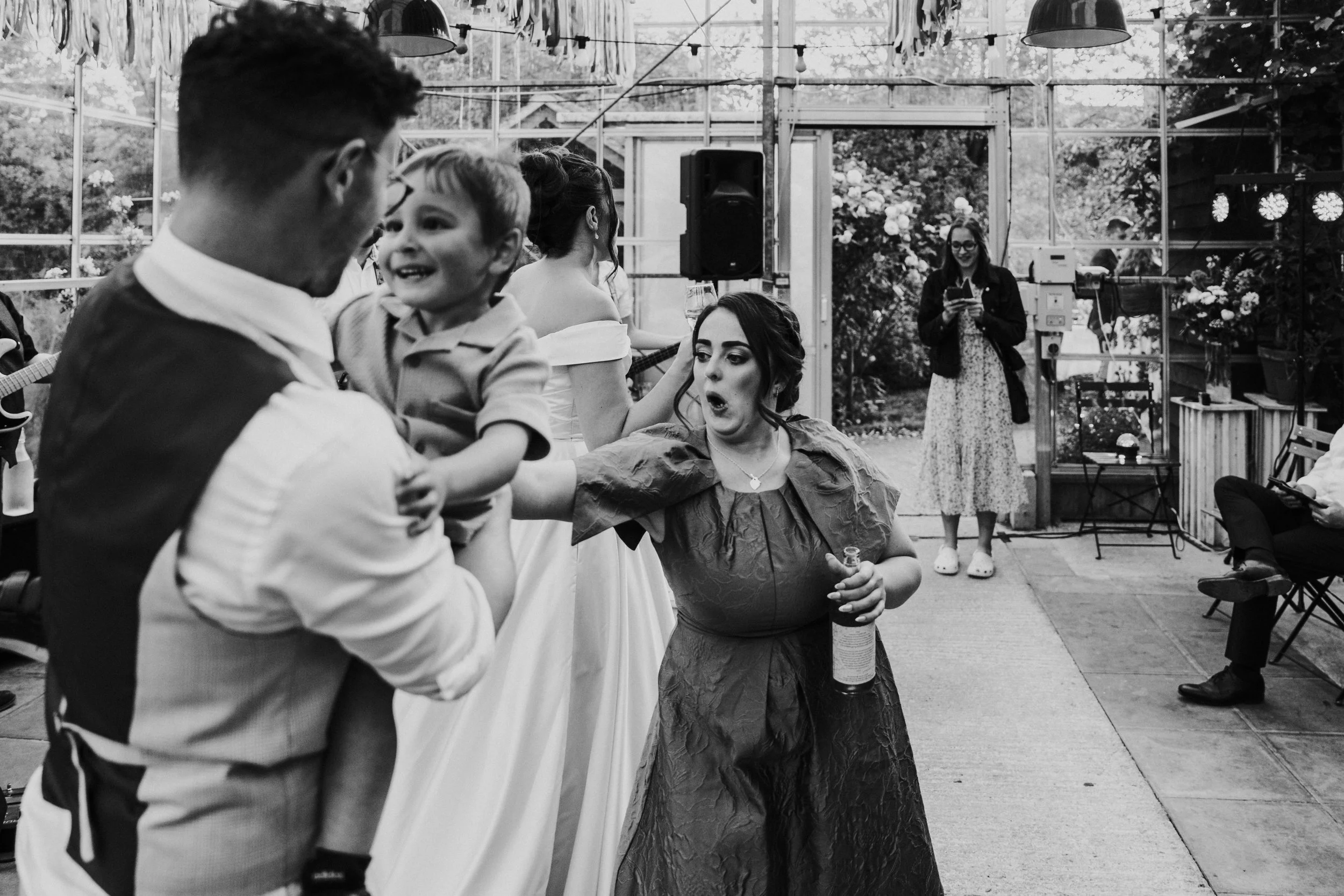 Groom holding baby while the bridesmaid point with a shock look at a Worton Kitchen Garden, Oxfordshire Wedding.